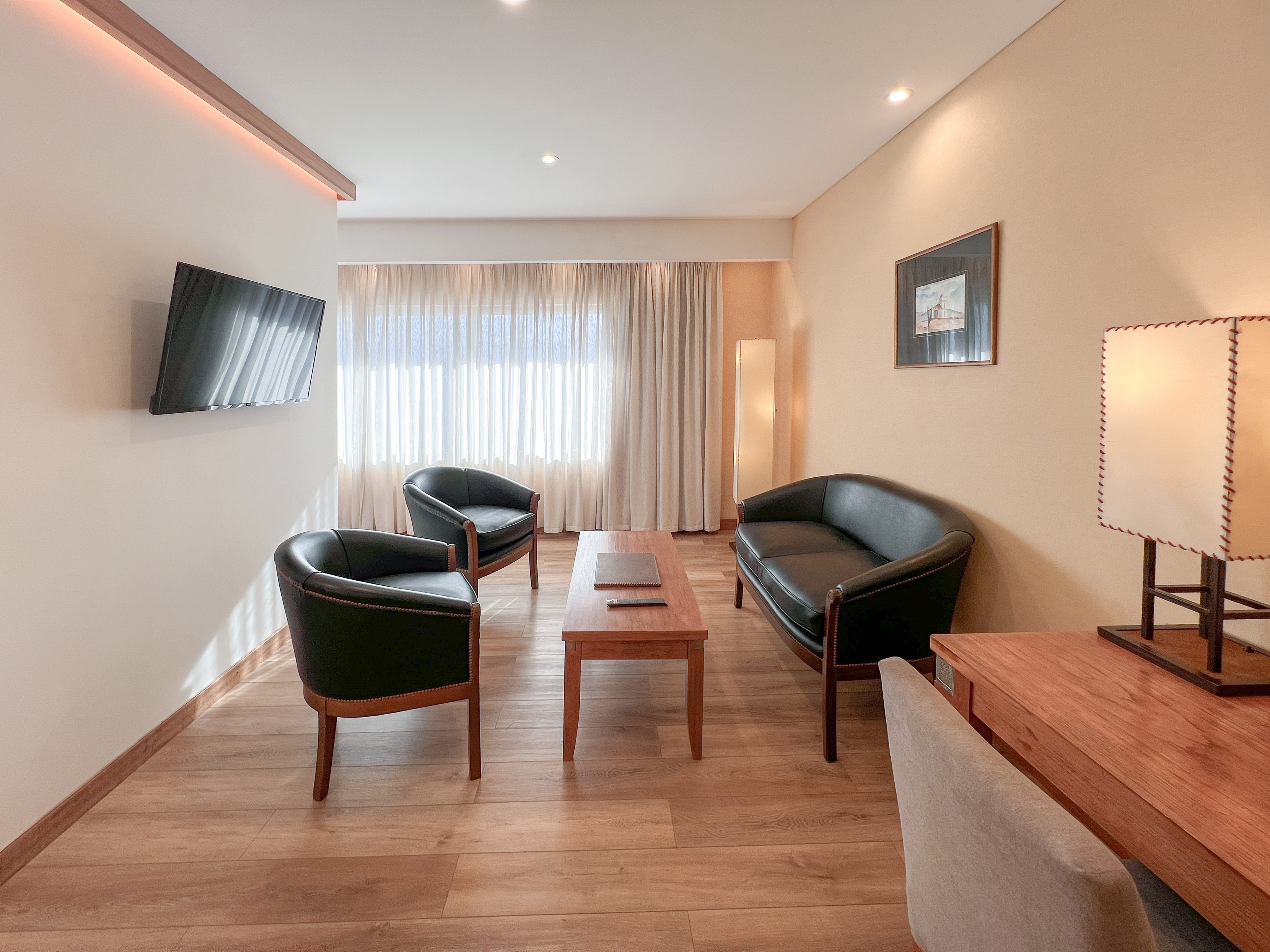 Modern hotel suite living room with leather furniture, wood floor, and TV.