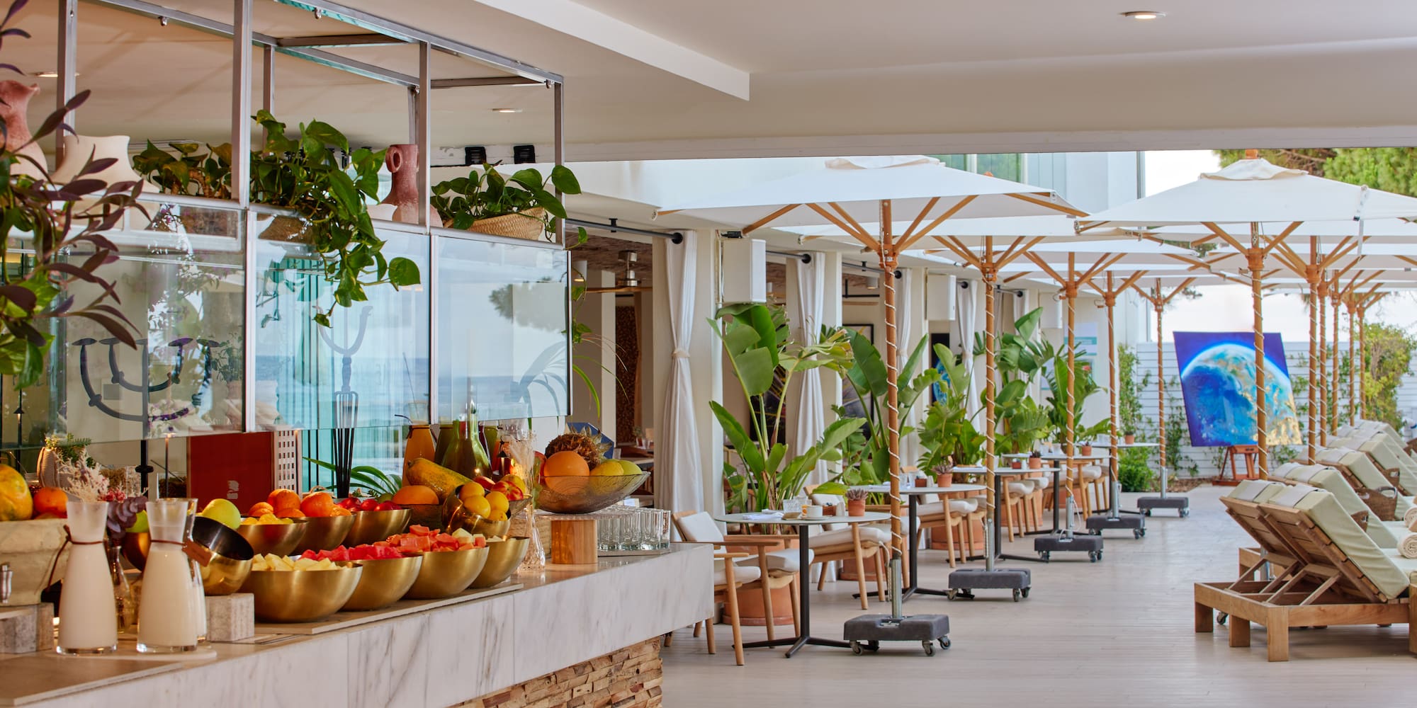 Resort outdoor dining: fresh fruit counter, patio tables, white umbrellas, lounge chairs.