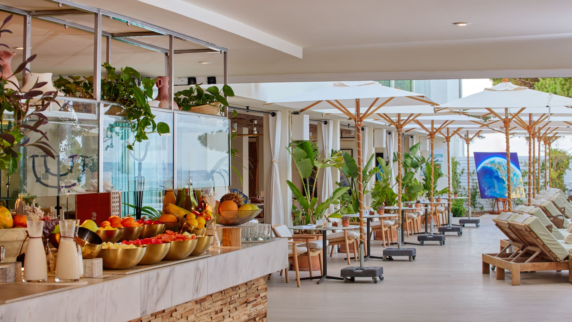 Resort outdoor dining: fresh fruit counter, patio tables, white umbrellas, lounge chairs.