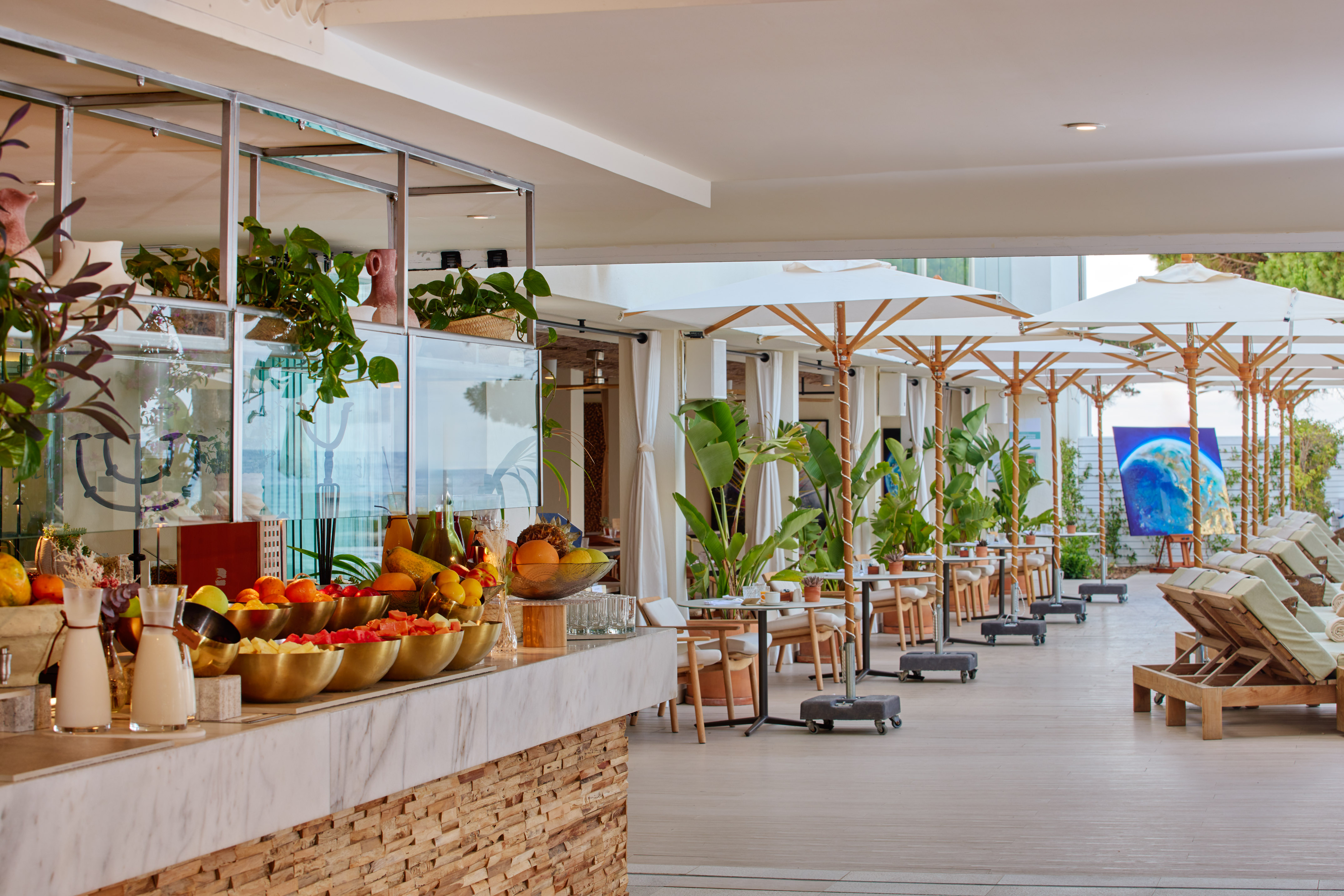 Resort outdoor dining: fresh fruit counter, patio tables, white umbrellas, lounge chairs.
