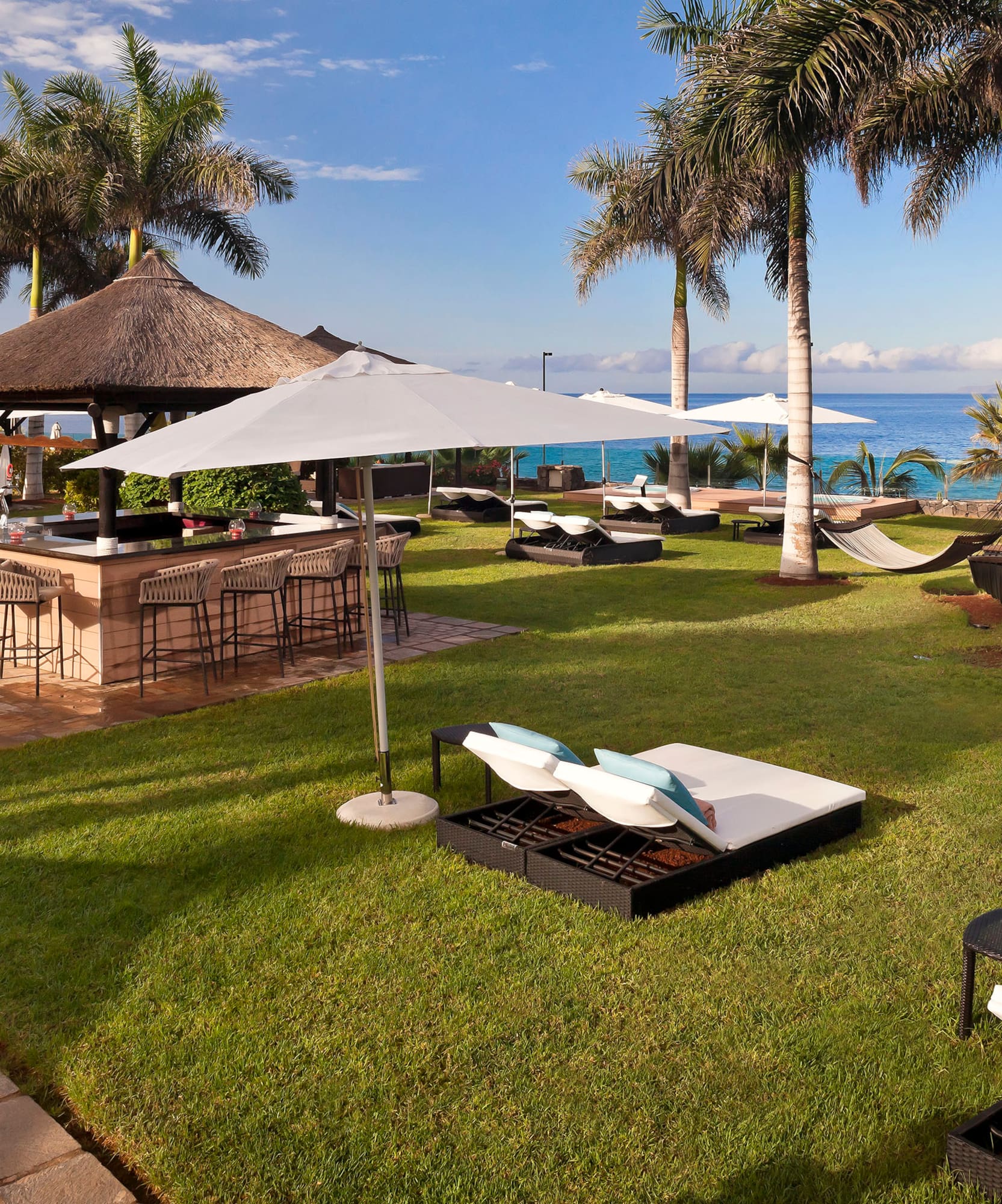 Resort outdoor bar with palm trees, lounge chairs, hammocks, and ocean view.