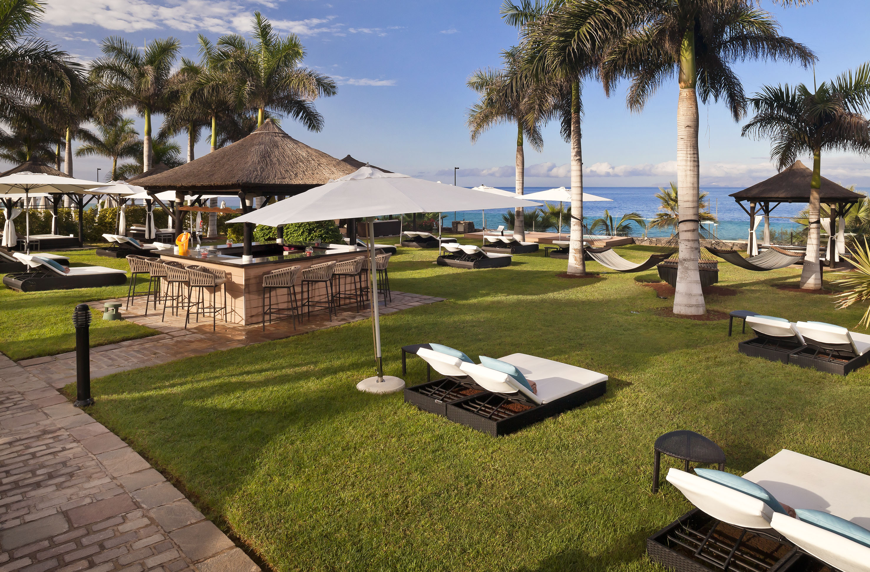 Resort outdoor bar with palm trees, lounge chairs, hammocks, and ocean view.