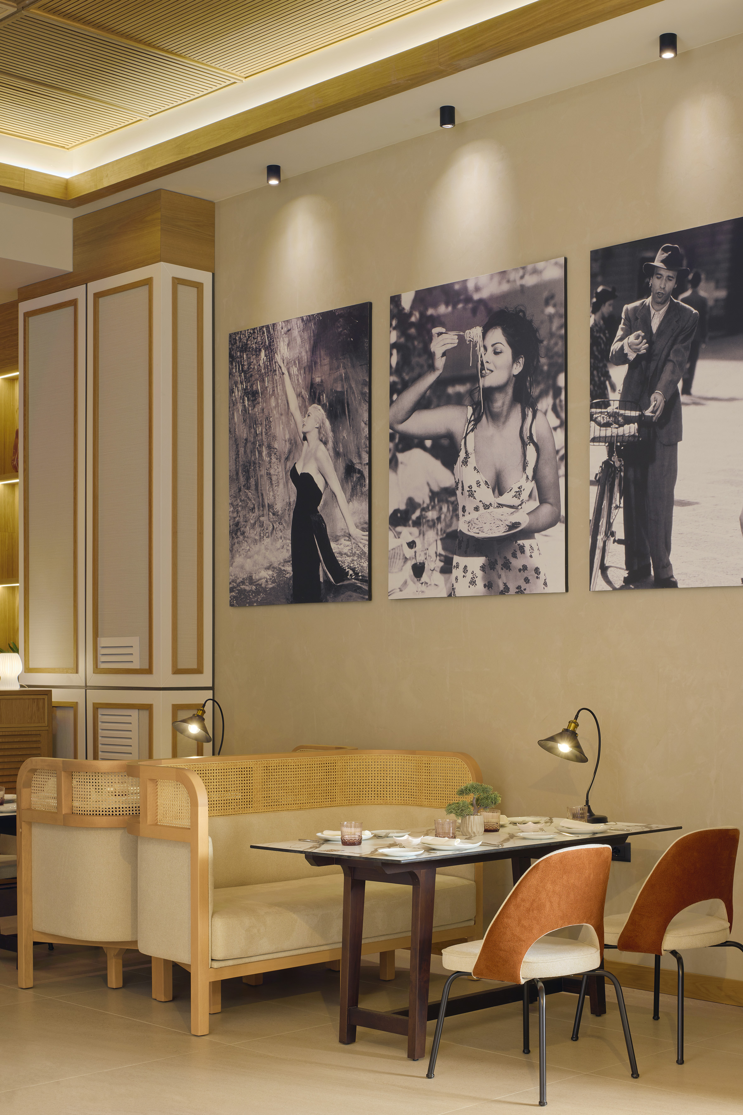 Modern restaurant interior with rattan booths, dining tables, and classic wall art.