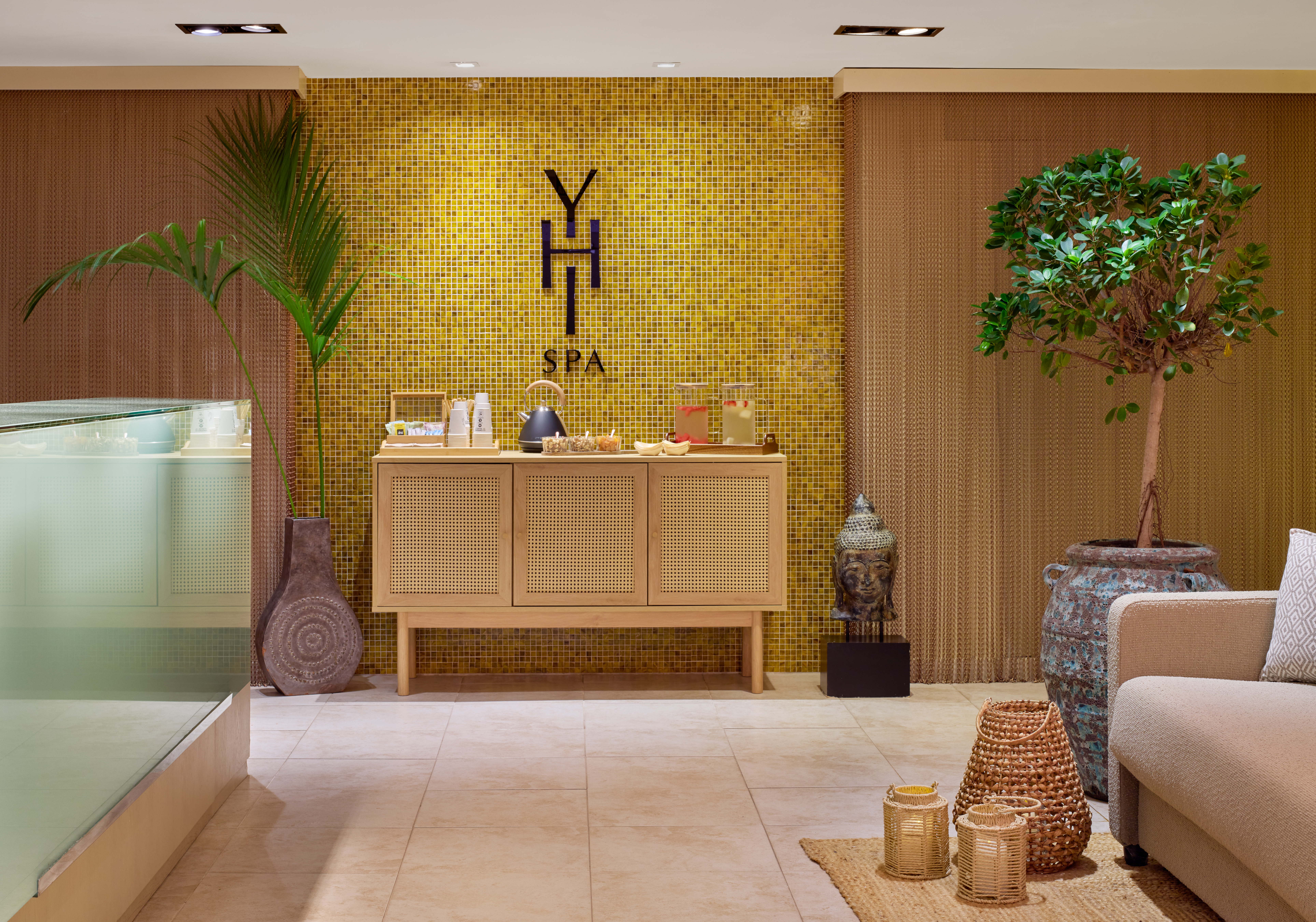 Relaxing spa waiting area with yellow mosaic wall, refreshments, plants, Buddha.