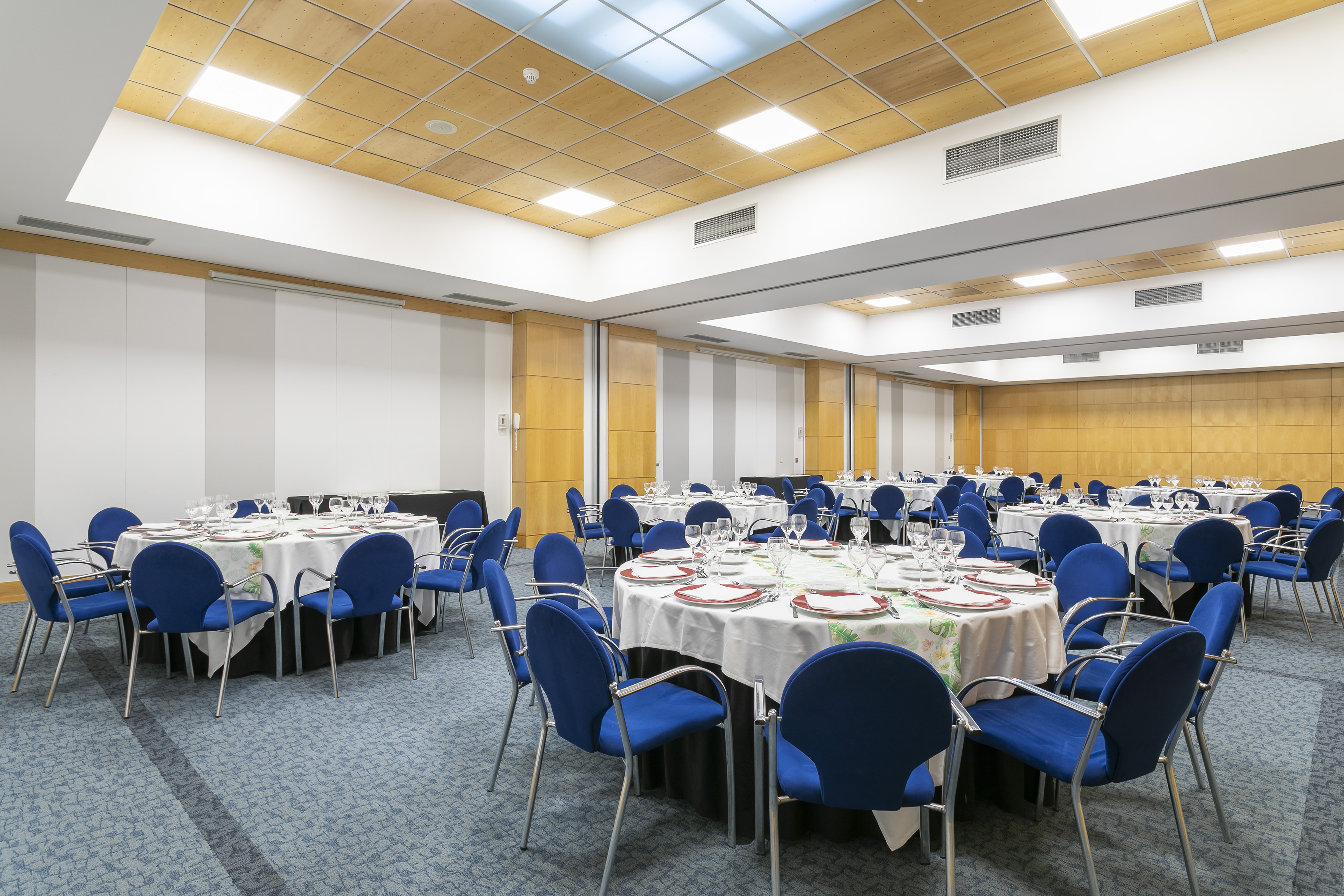 Banquet hall with round tables, blue chairs, full place settings, and wood ceiling.