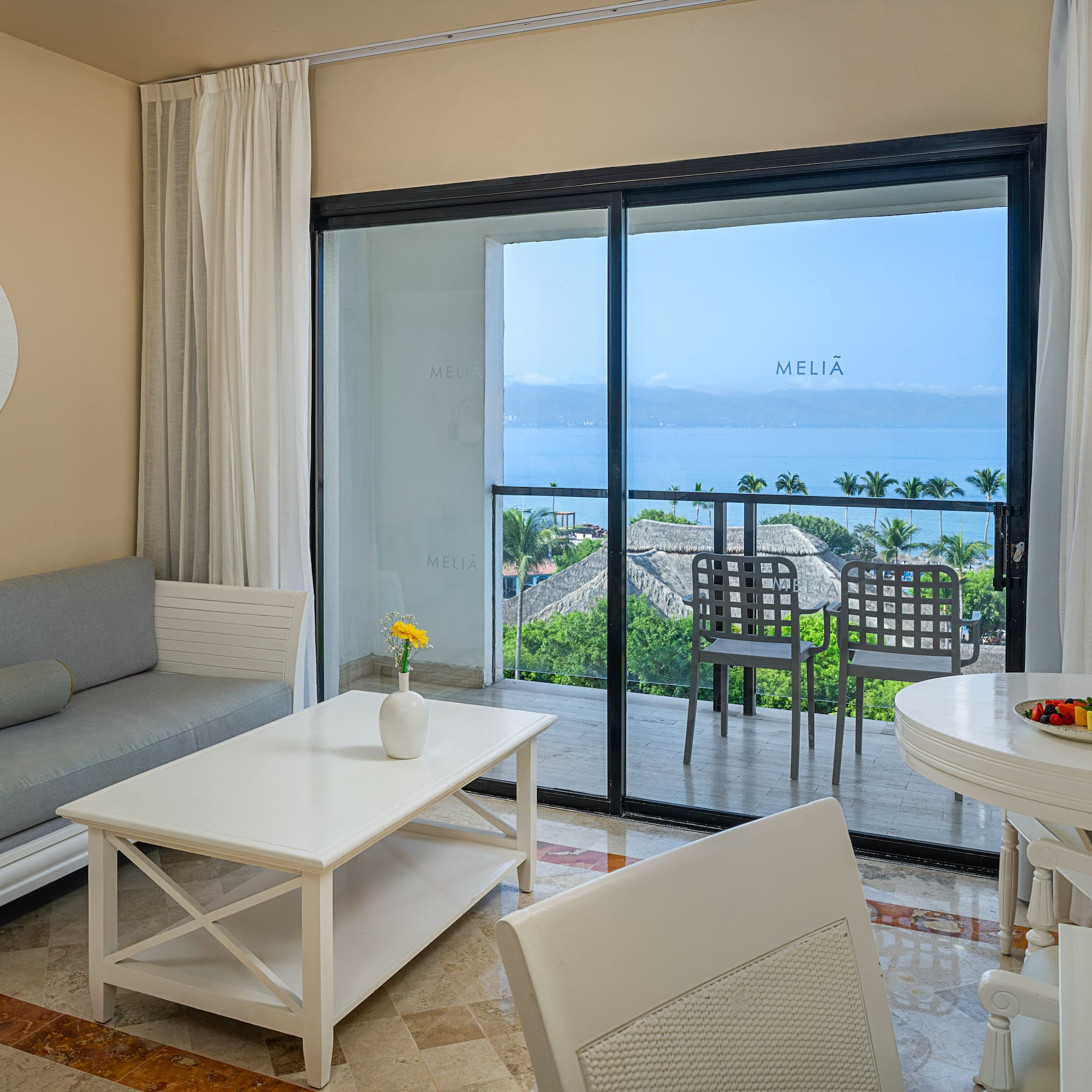 Hotel suite with ocean view balcony, living and dining areas.