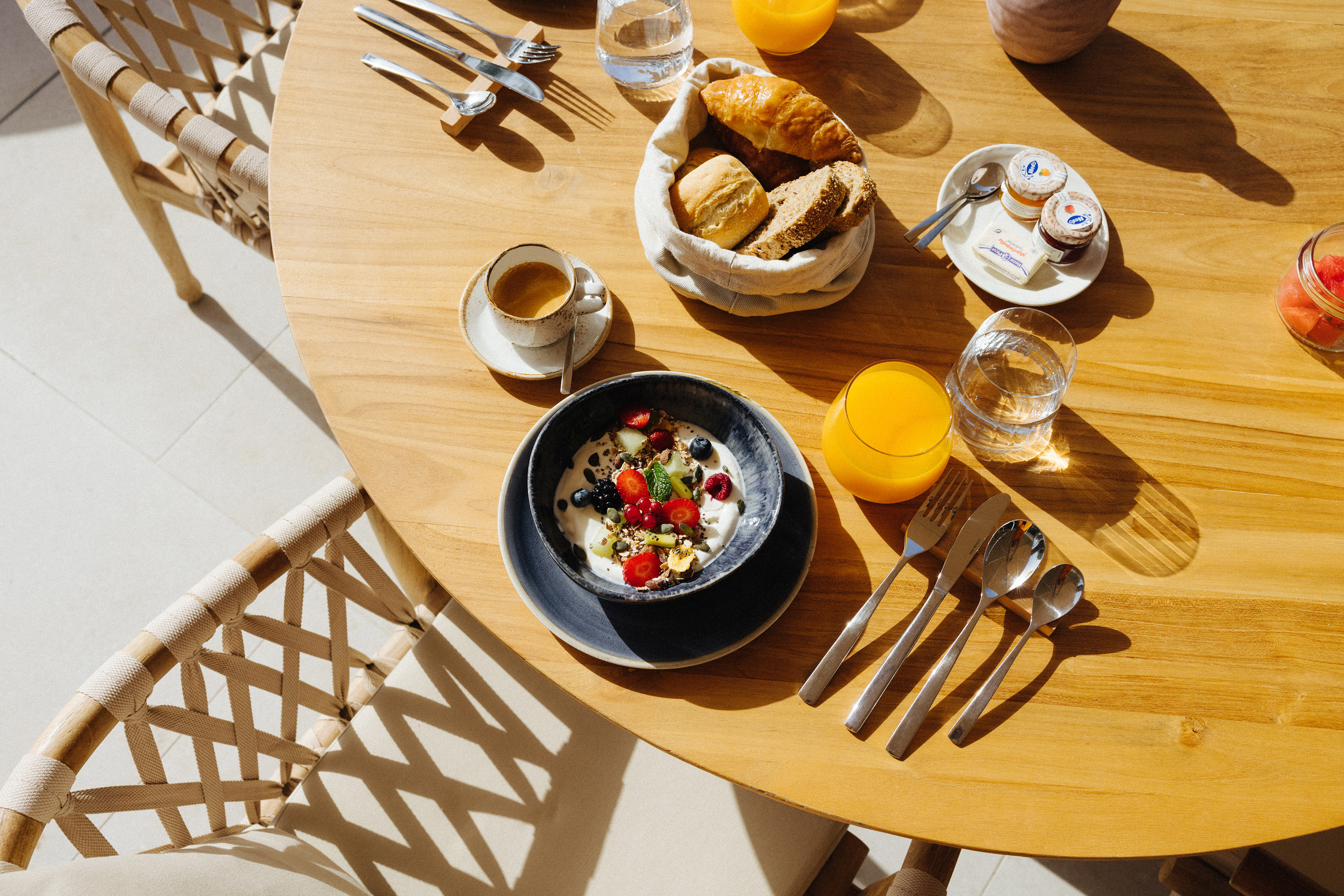 Sunny breakfast on wooden table with yogurt, berries, coffee, juice, bread.