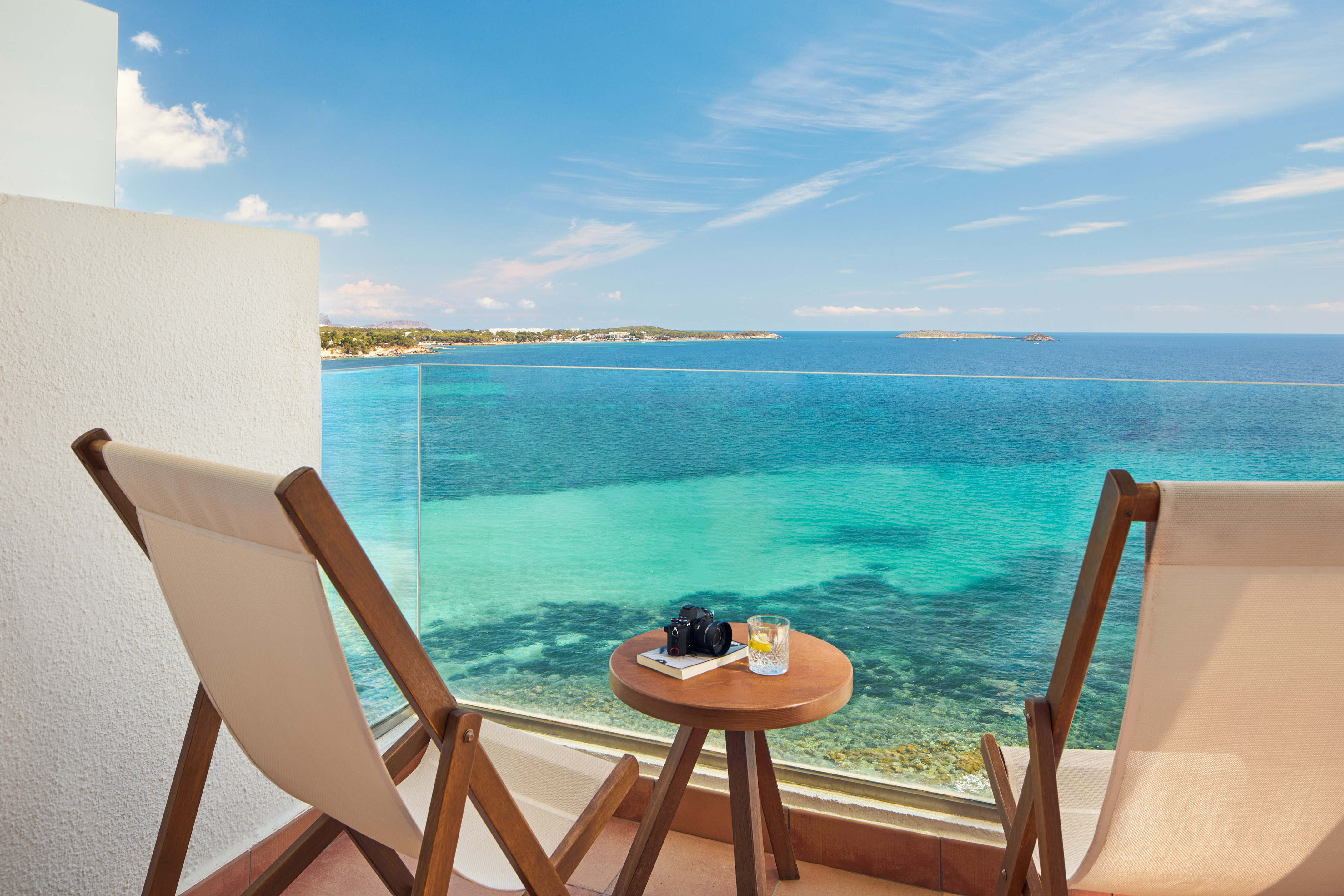 Oceanfront balcony with two lounge chairs, table, and clear turquoise sea.