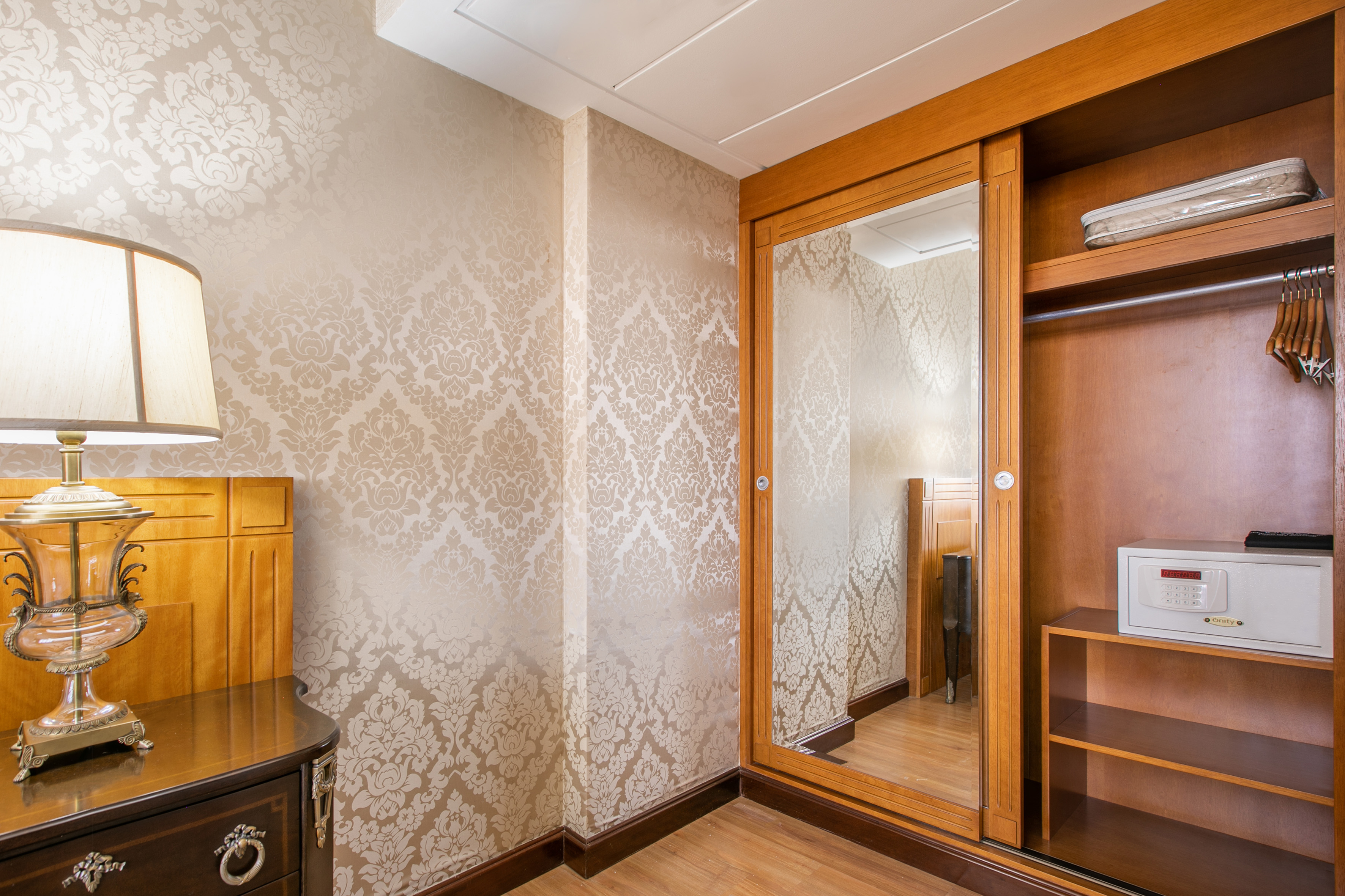 Hotel room interior with damask wallpaper, wooden closet, mirror, and security safe.