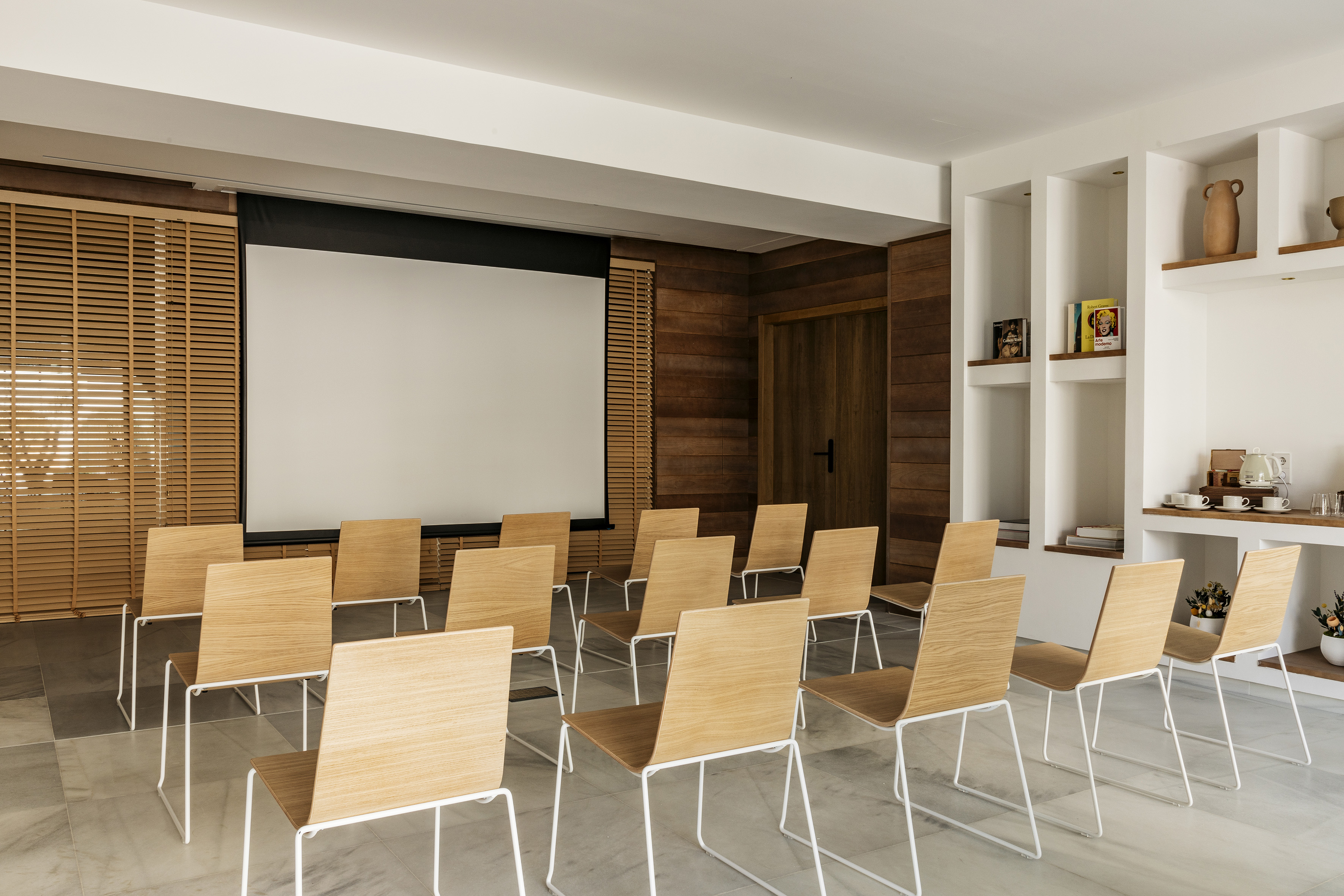 Modern conference room with projector screen, wood chairs, and a coffee station.
