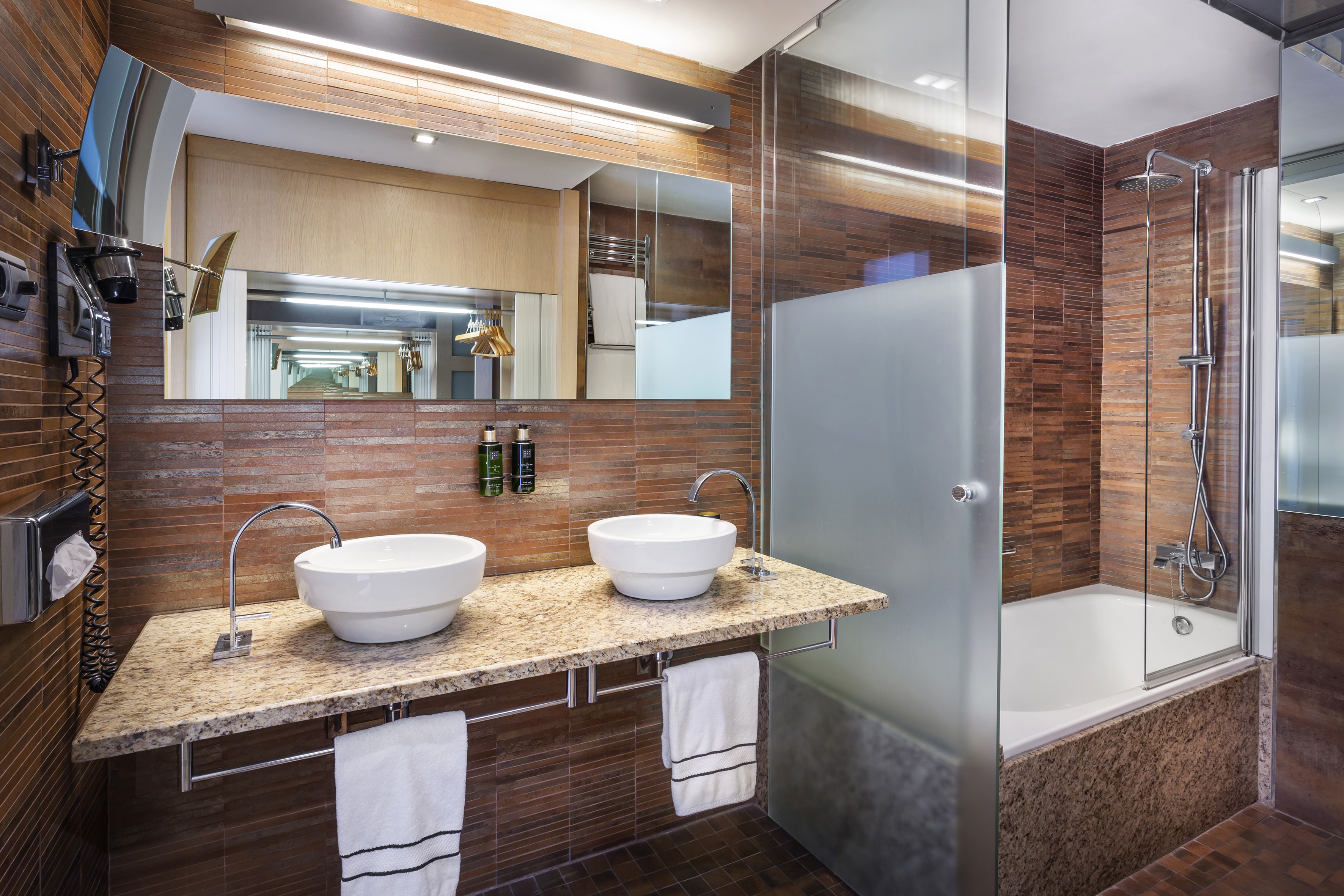 Baño moderno con doble lavabo, azulejos terracota y ducha de cristal.
