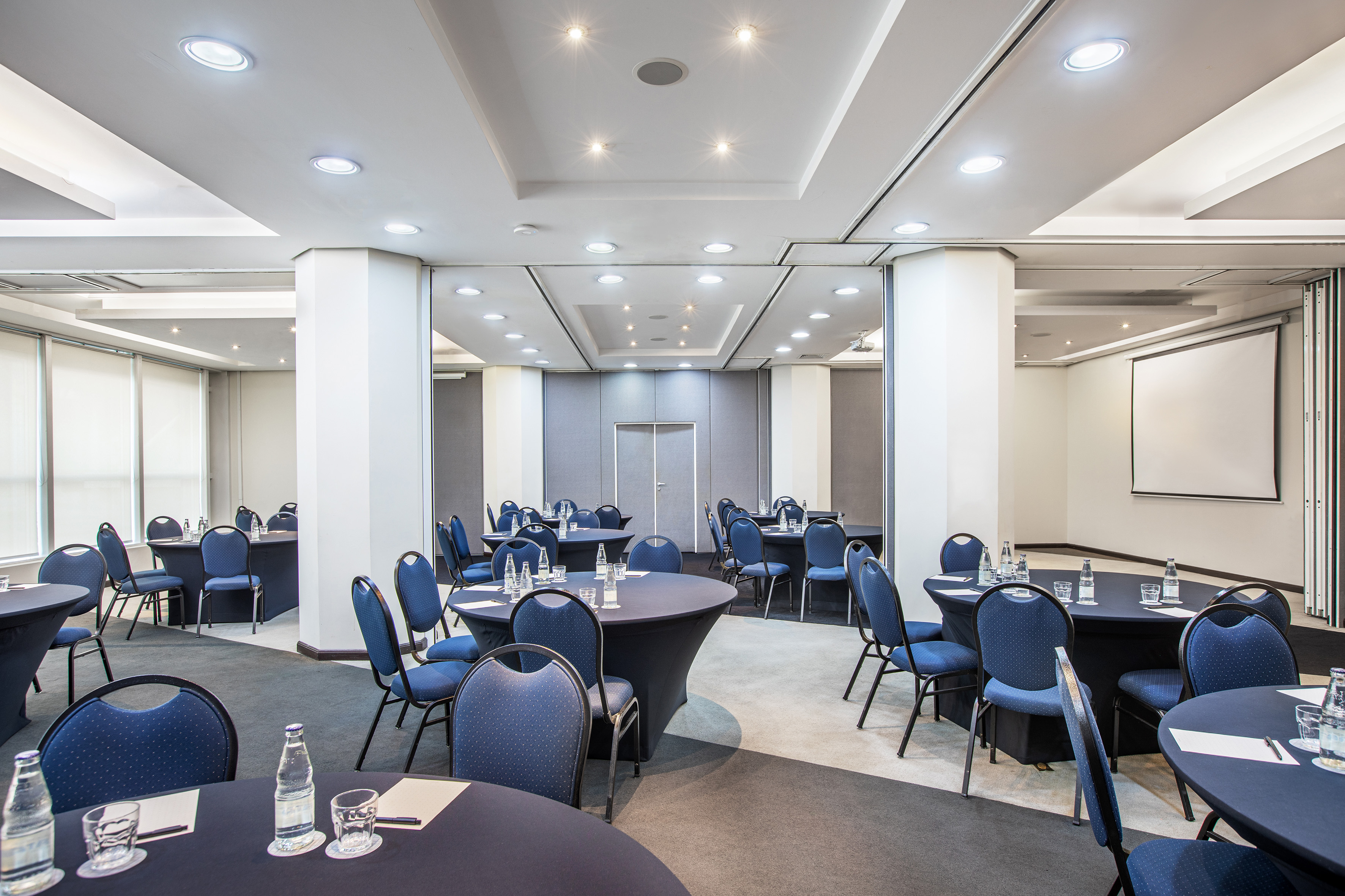 Modern meeting room with round tables, blue chairs, and presentation screen.