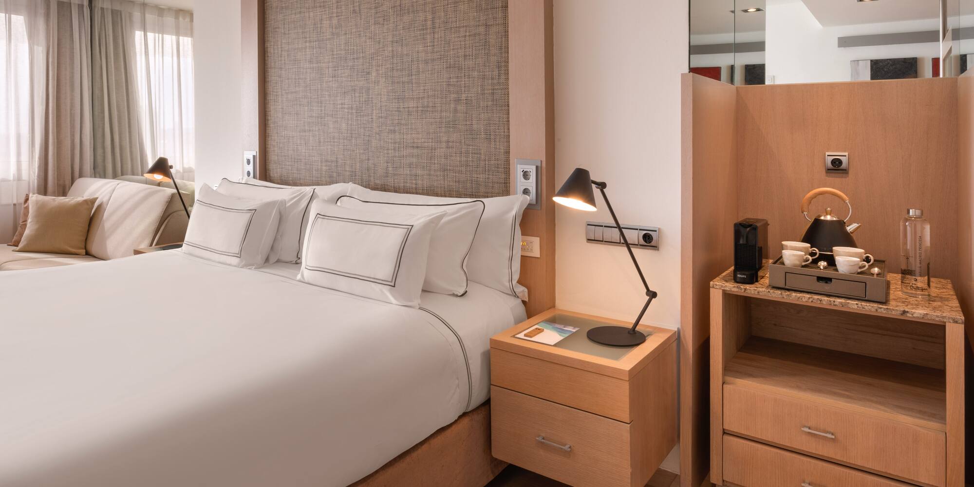 Modern hotel bedroom with white king bed, wooden accents, and coffee machine.