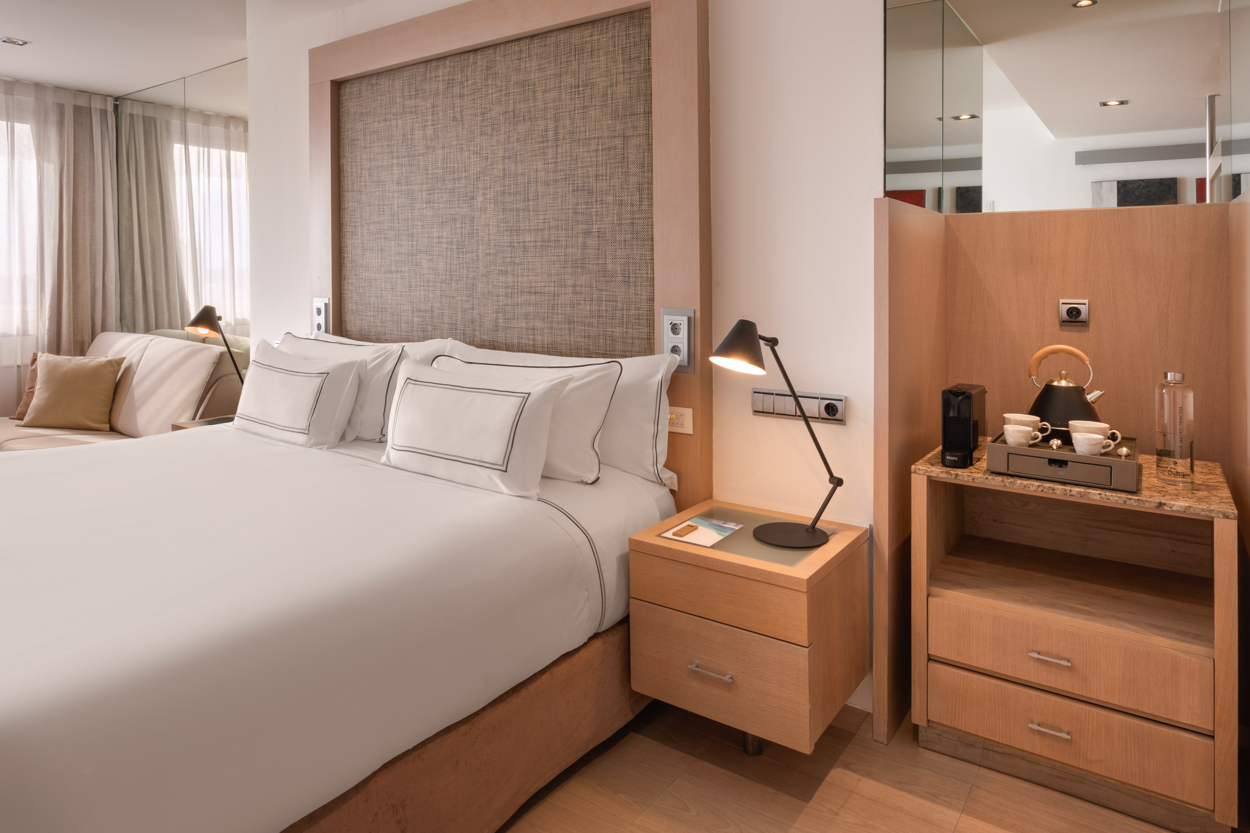 Modern hotel bedroom with white king bed, wooden accents, and coffee machine.