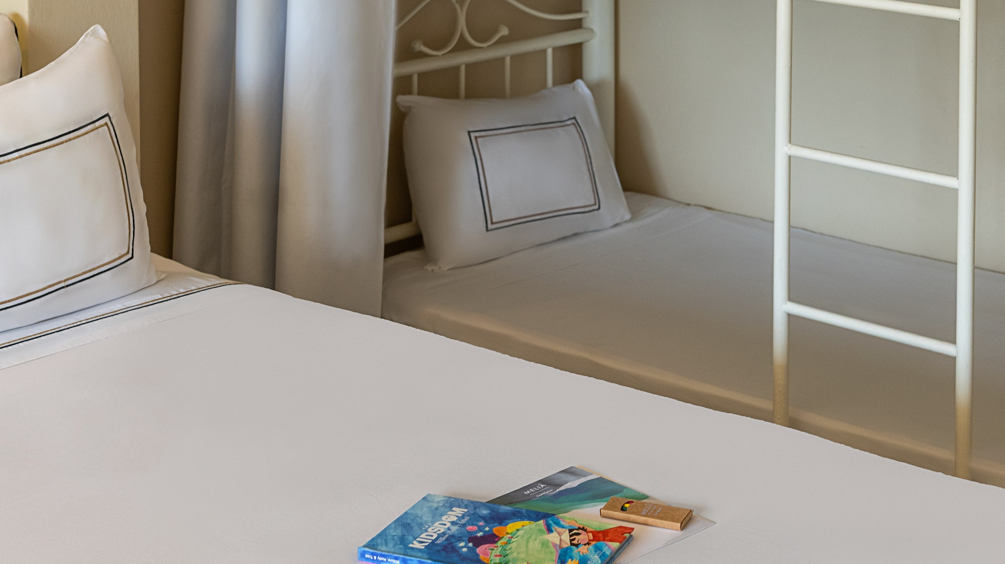 Family hotel room with bunk beds, white bedding, and Kidsdom activity kits.