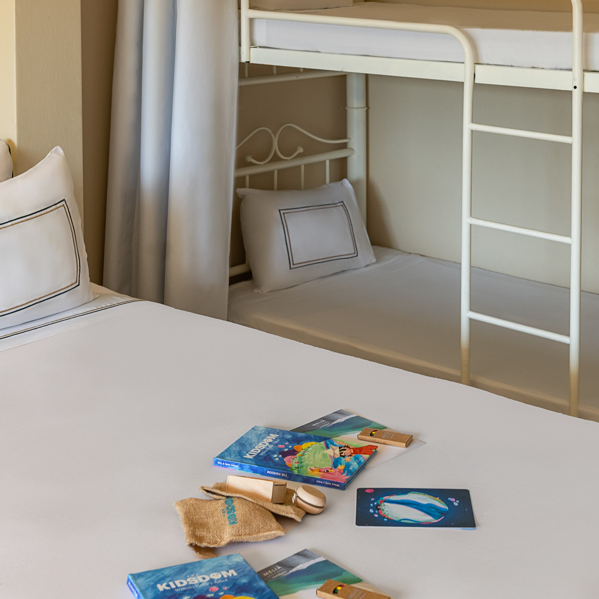 Family hotel room with bunk beds, white bedding, and Kidsdom activity kits.