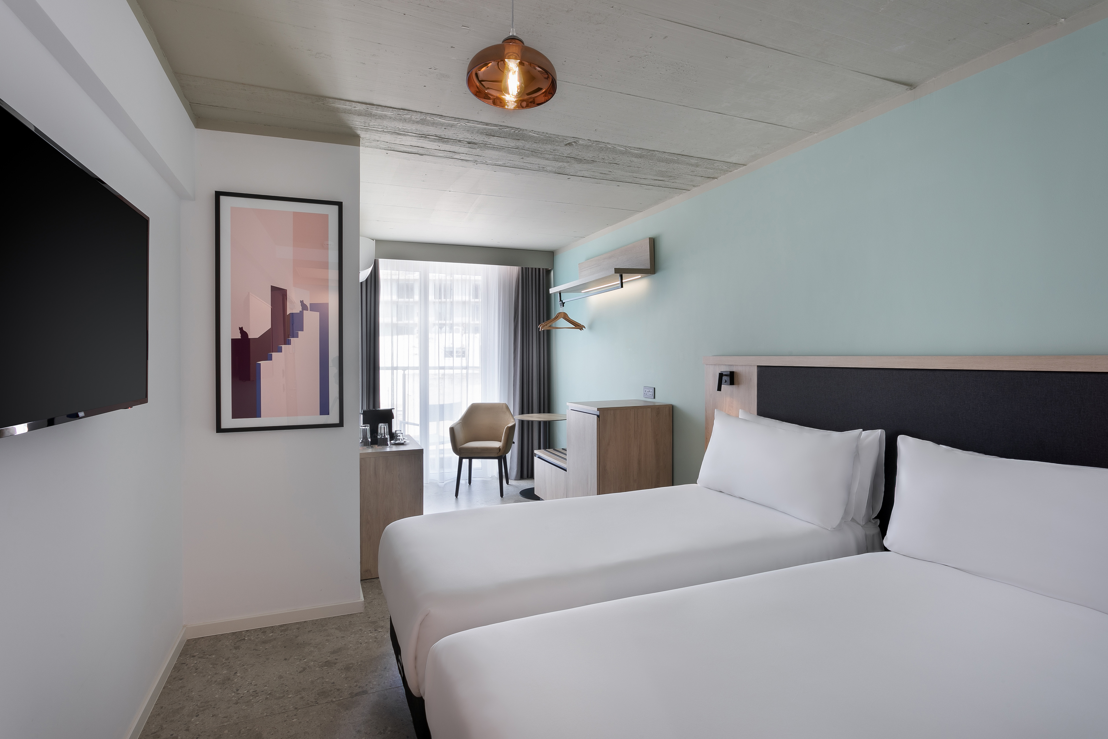 Modern hotel twin room with minimalist design, light blue wall, and concrete ceiling.