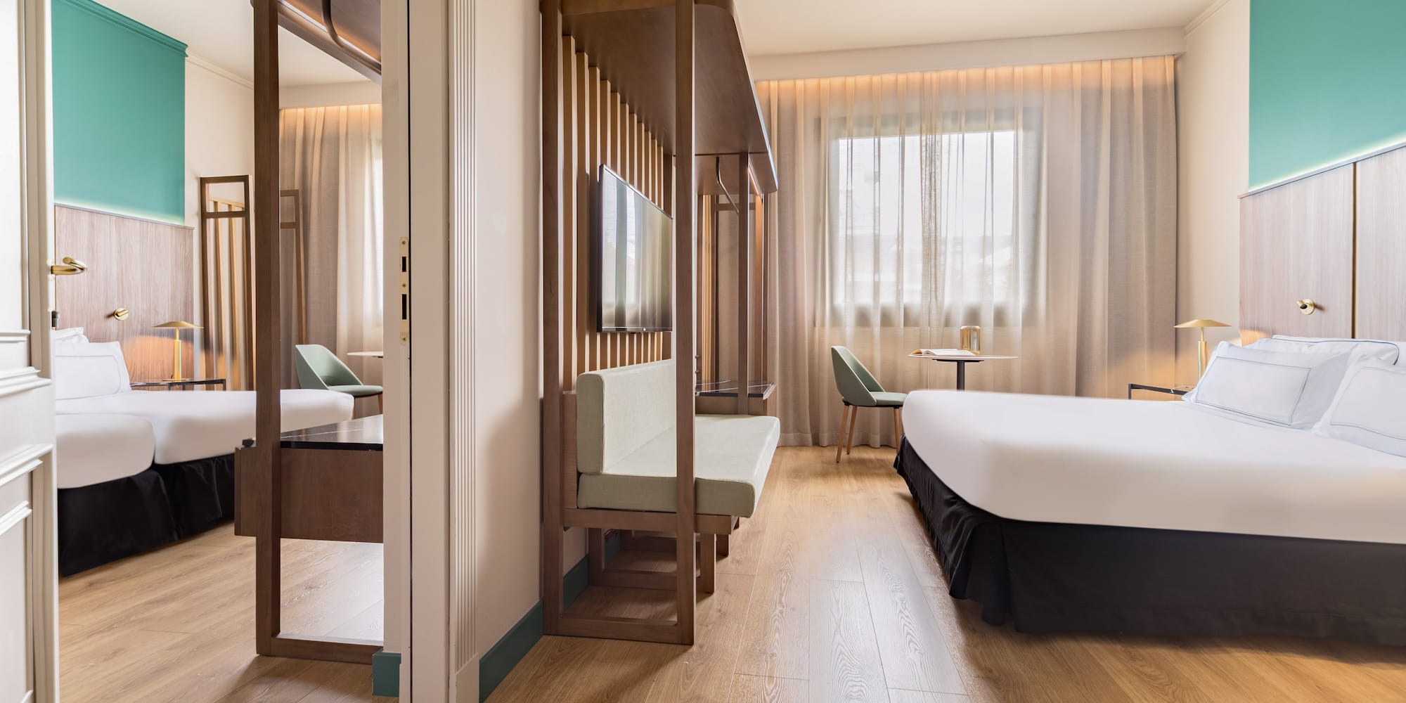 Modern hotel room with wood floor, teal accent wall, bed, and slatted partition.