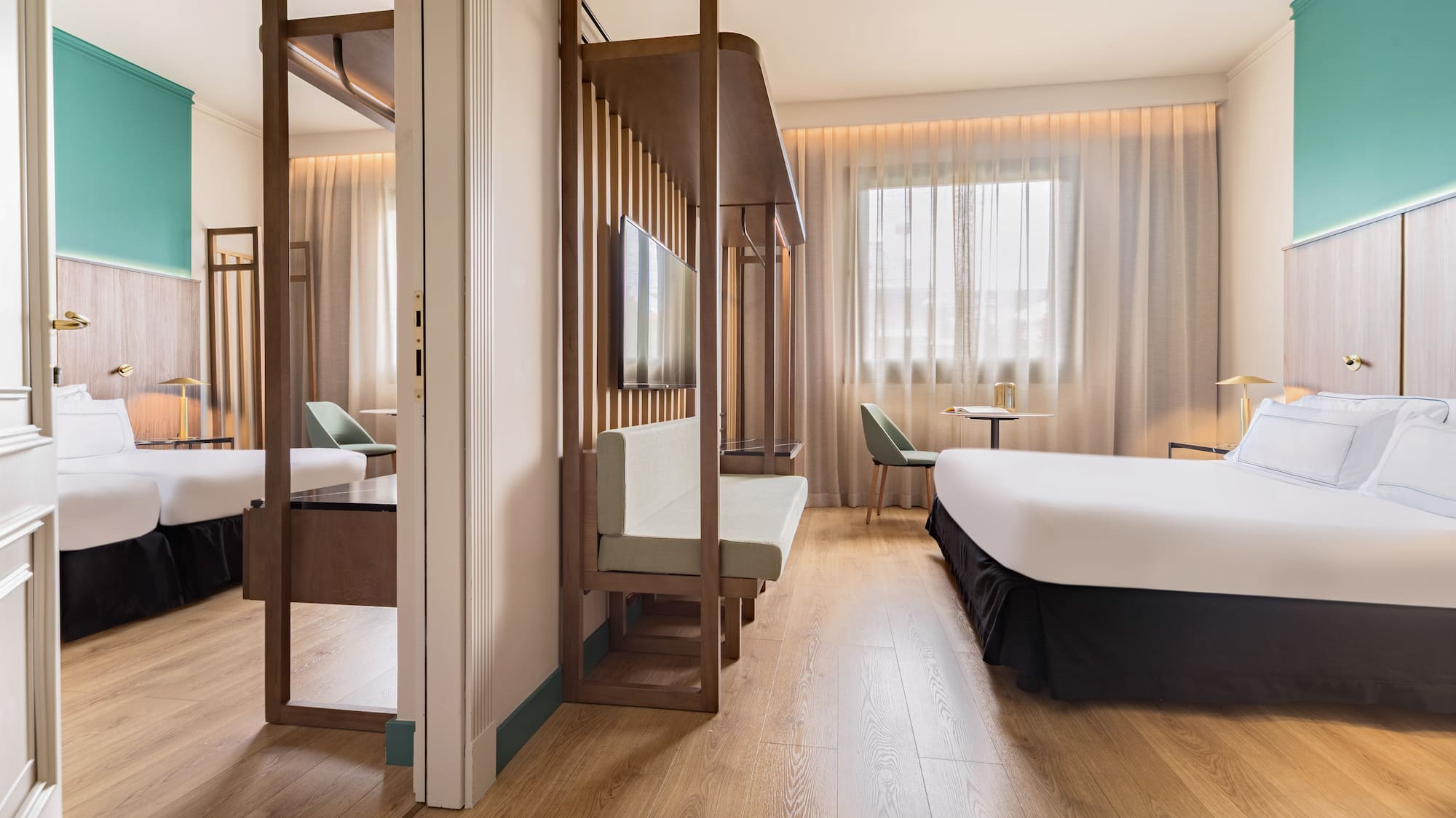 Modern hotel room with wood floor, teal accent wall, bed, and slatted partition.