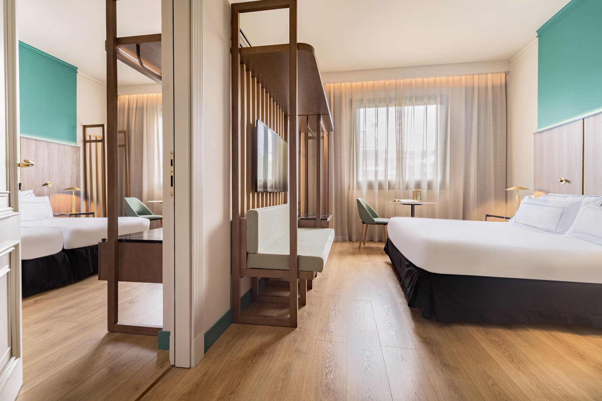 Modern hotel room with wood floor, teal accent wall, bed, and slatted partition.