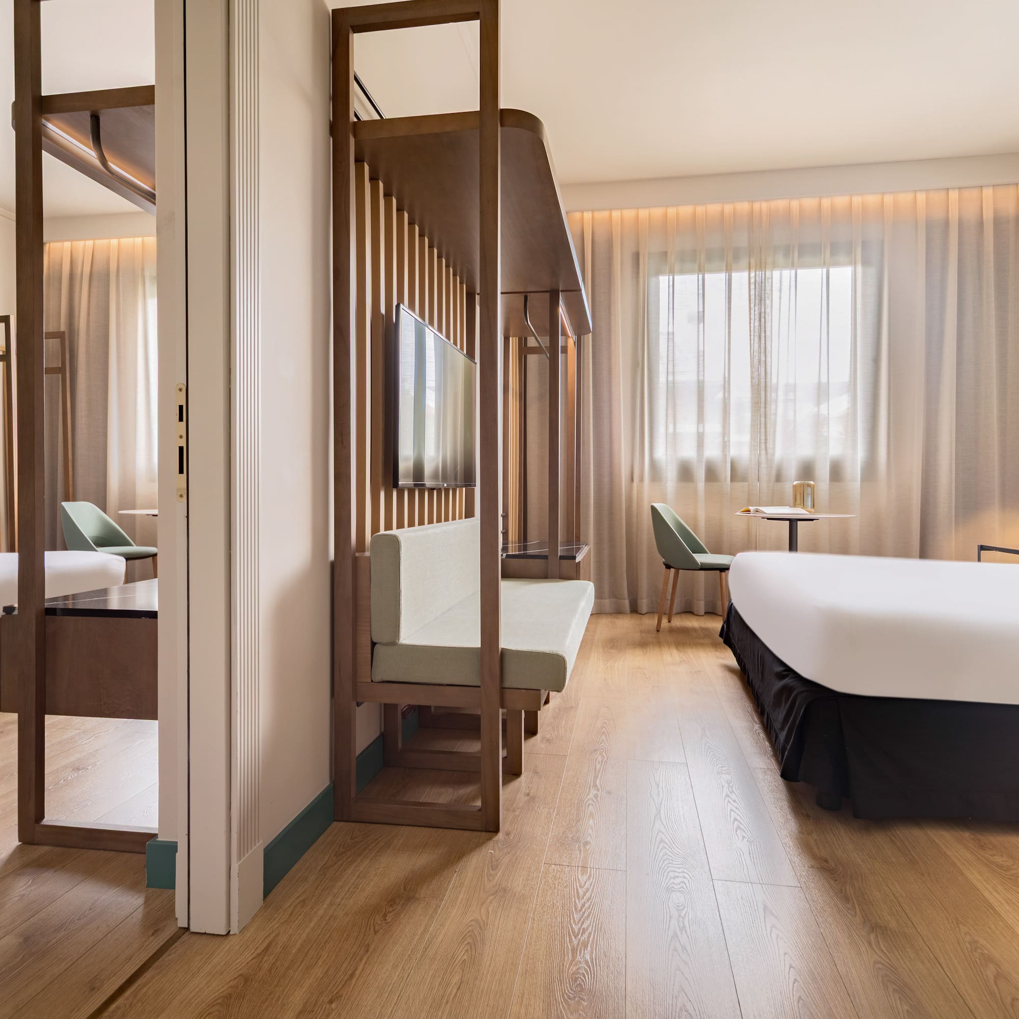 Modern hotel room with wood floor, teal accent wall, bed, and slatted partition.