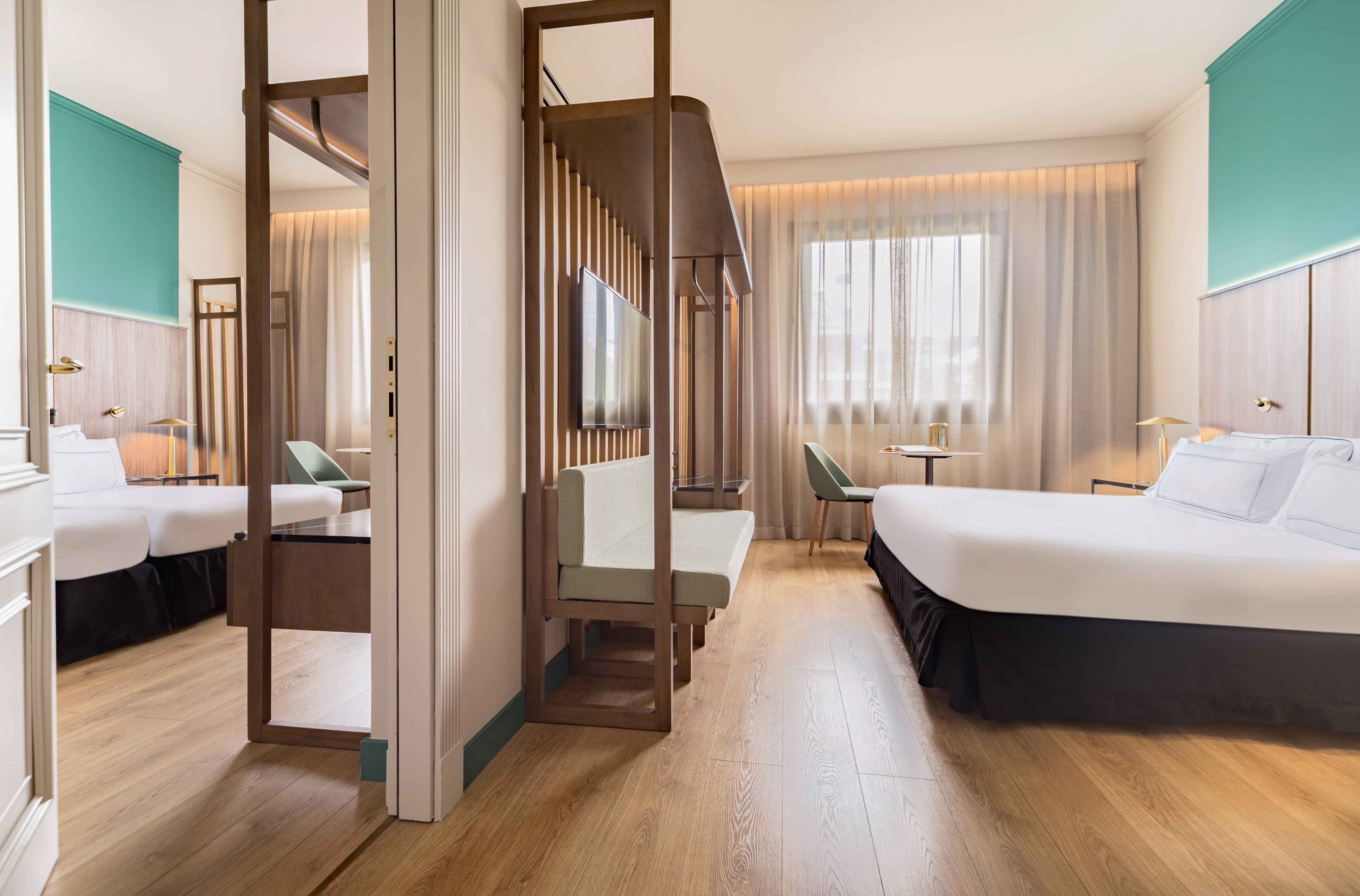 Modern hotel room with wood floor, teal accent wall, bed, and slatted partition.