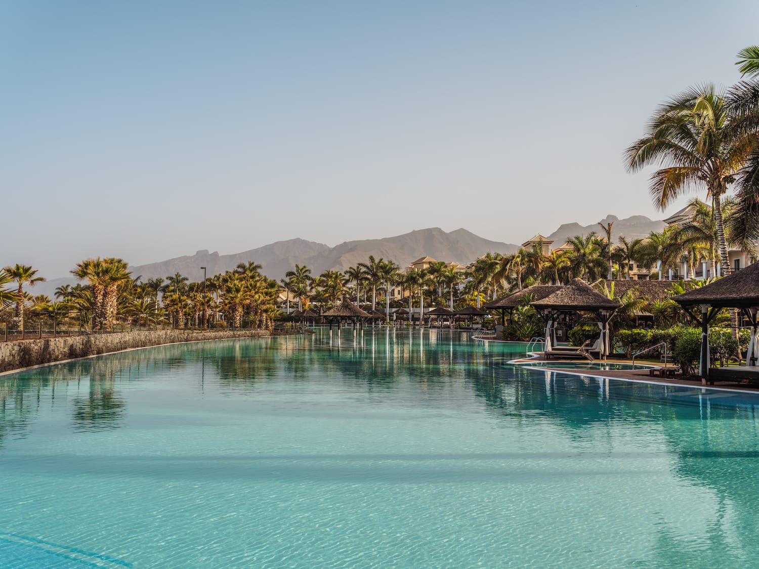 a pool with a large body of water and a large building with trees and mountains in the background