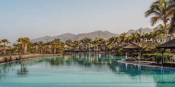 a pool with a large body of water and a large building with trees and mountains in the background