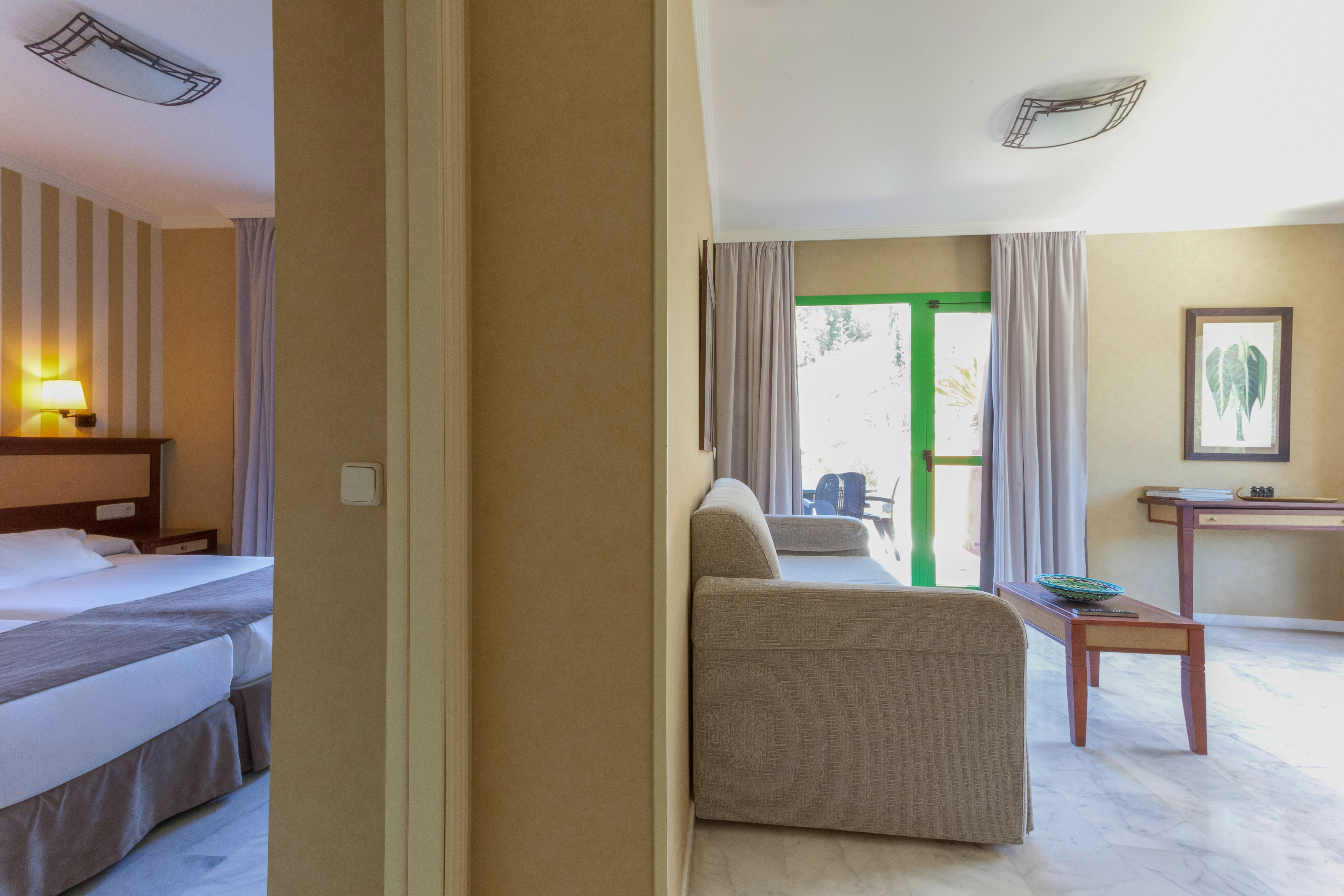 Hotel suite interior with bedroom, living room sofa, and green balcony door.