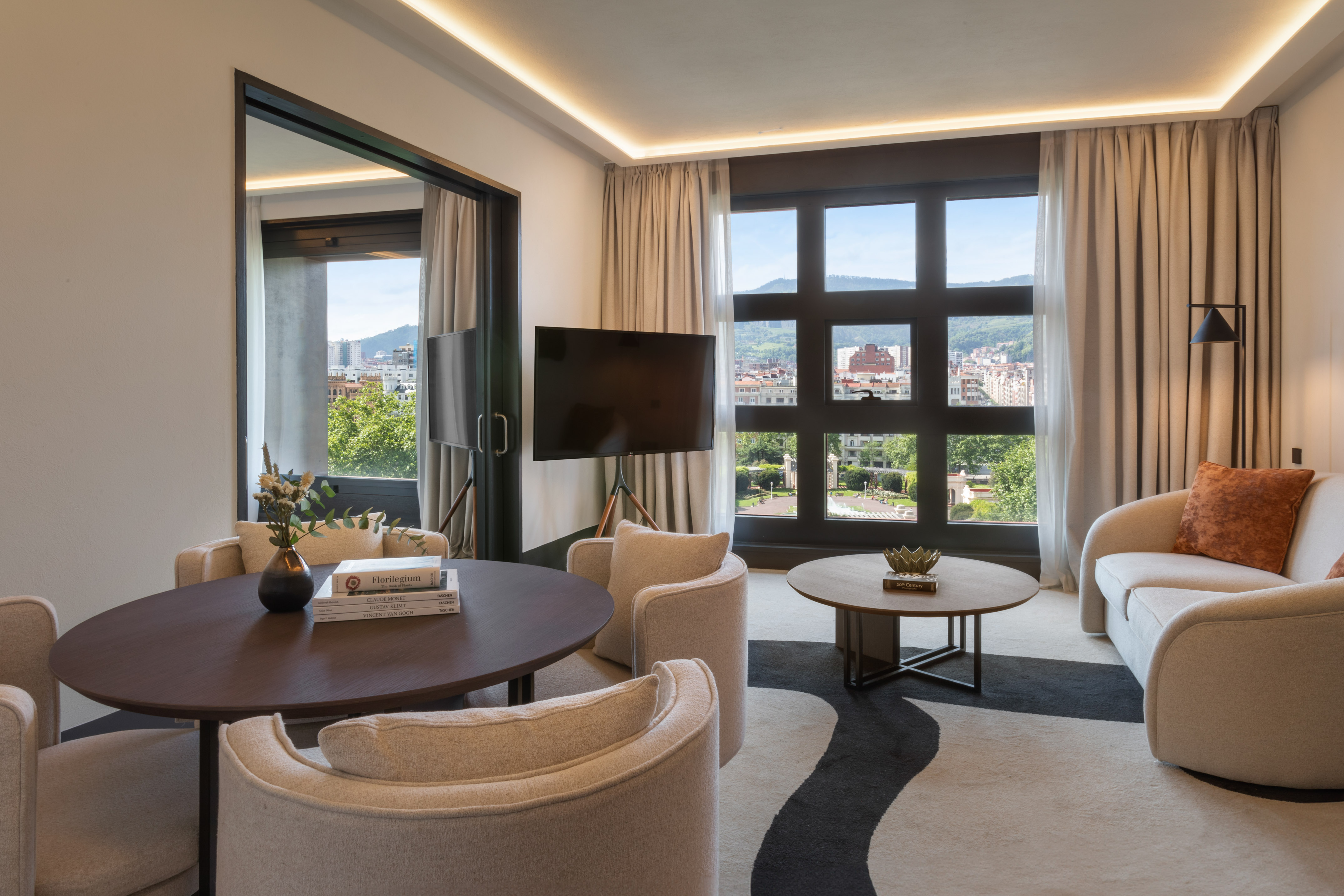 Stylish modern living room with city view, beige sofa, dining table, and TV.