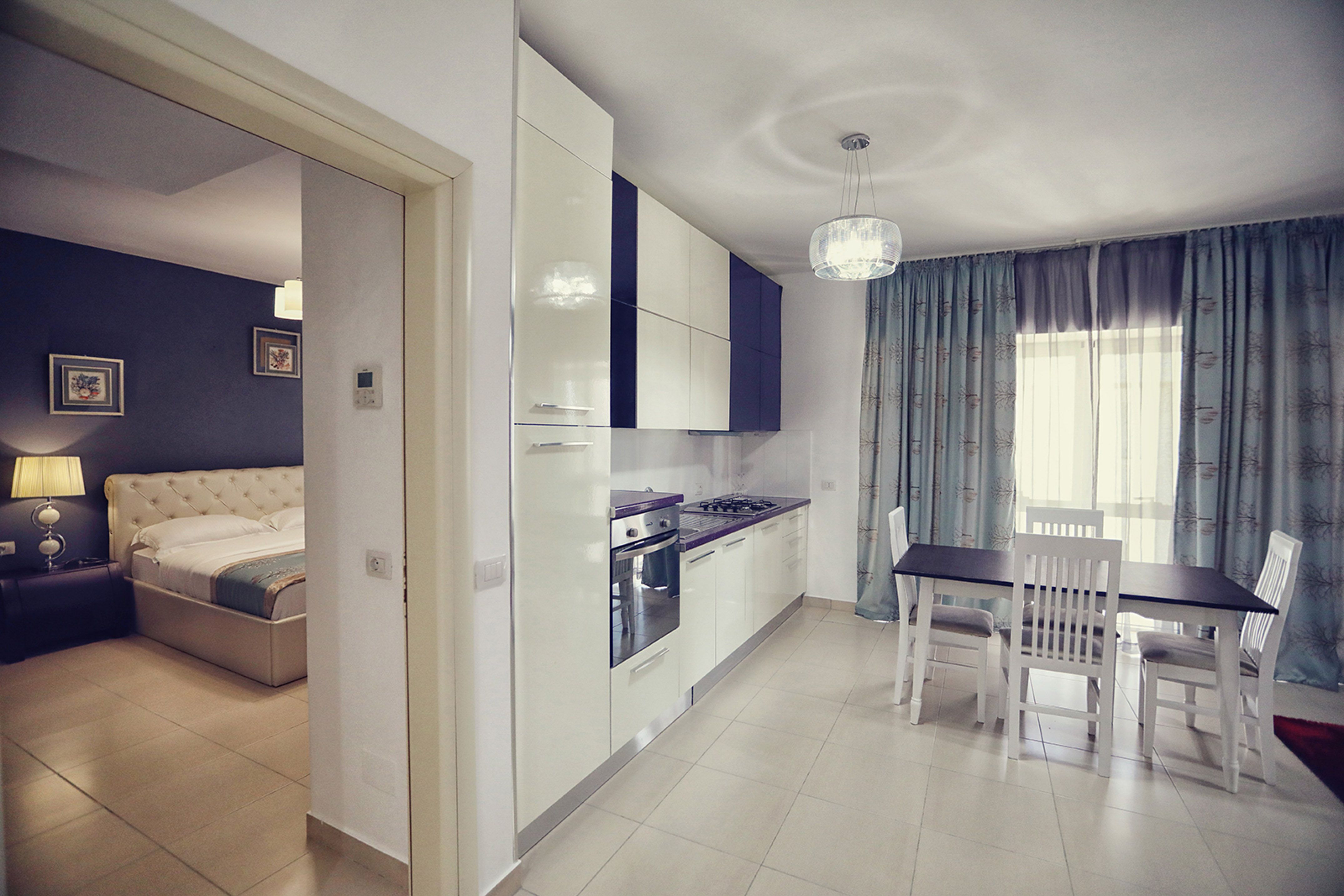 Open-plan apartment with cream kitchen, dining area, and bedroom glimpse.