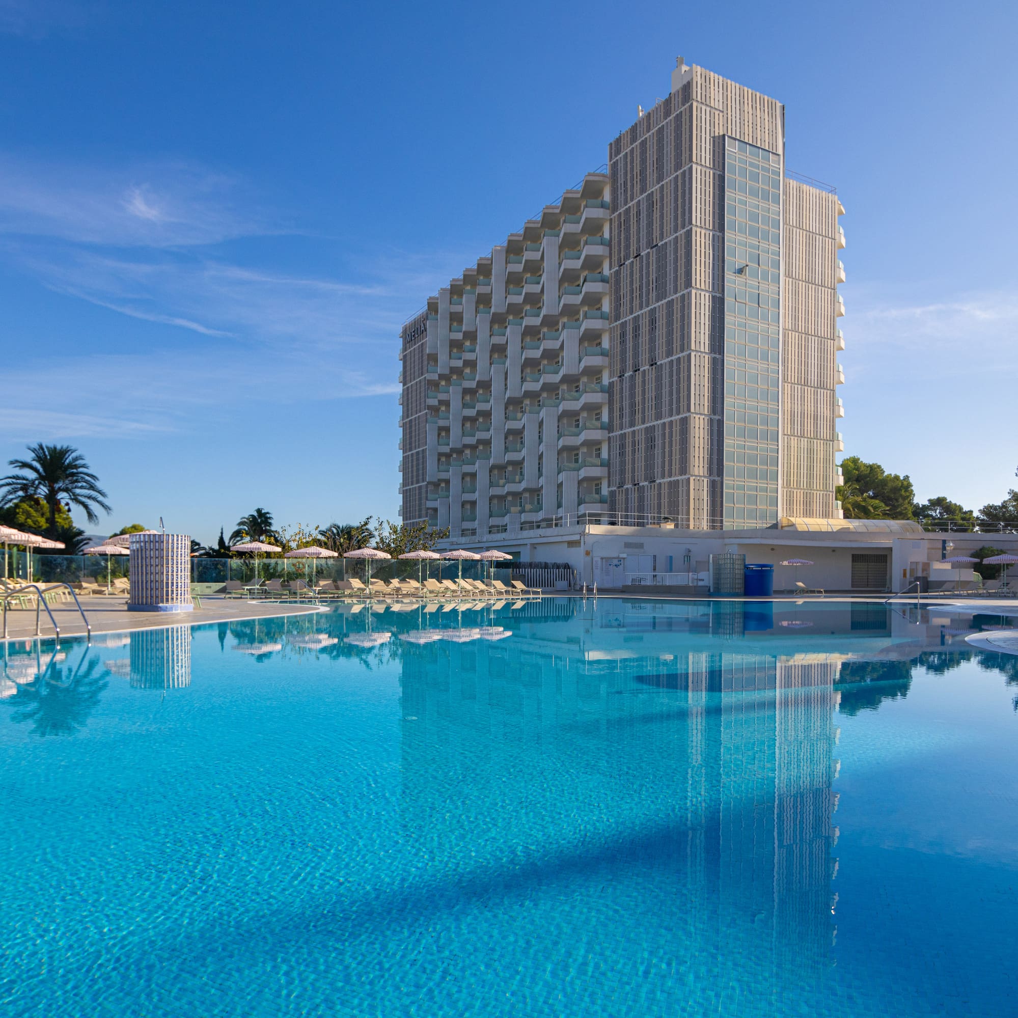 Sunny resort hotel with large outdoor swimming pool and lounge area.