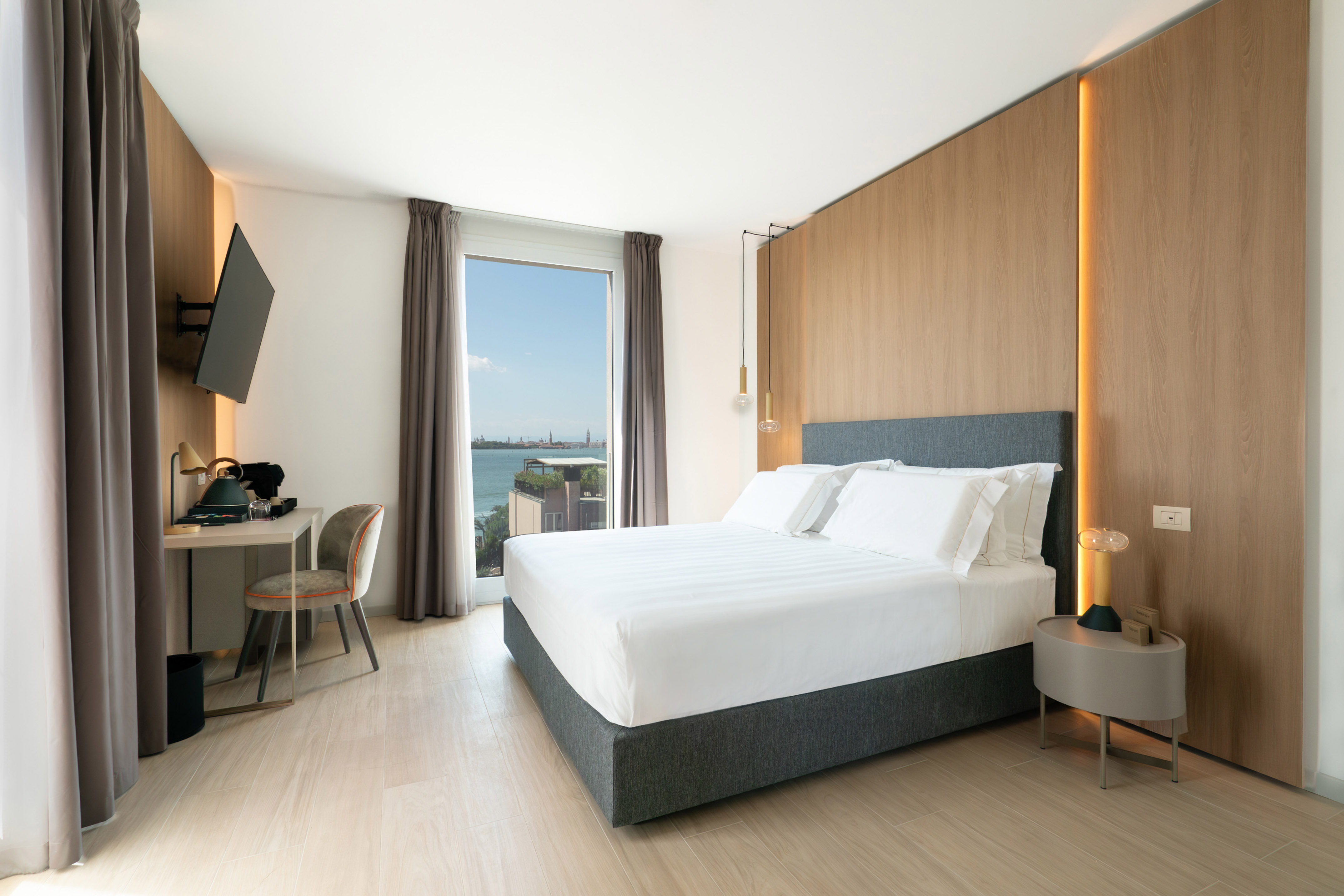 Contemporary bedroom with sea view, large bed, desk, and wood paneling.