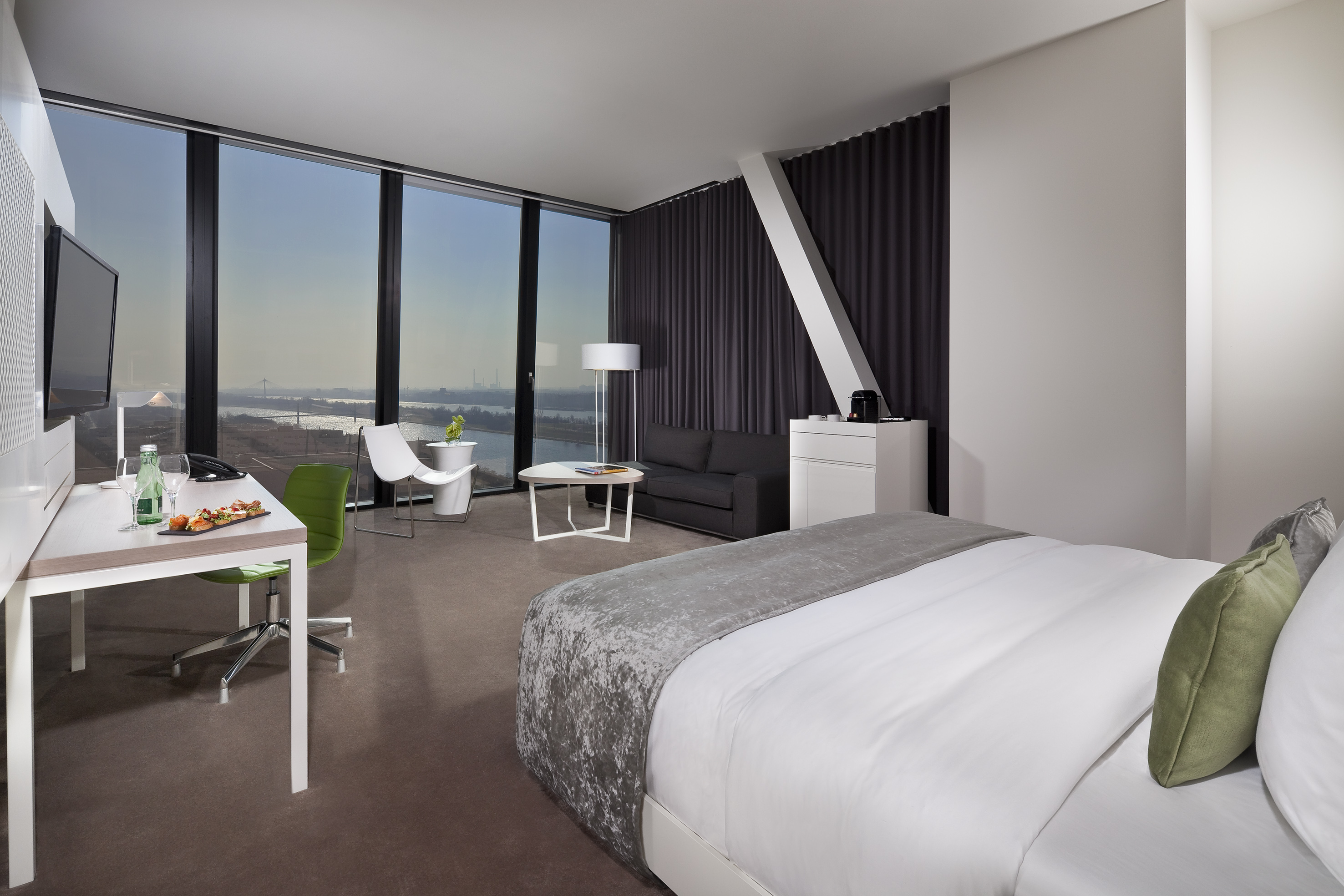 Modern hotel room with river view, comfortable bed, work desk, and lounge area.