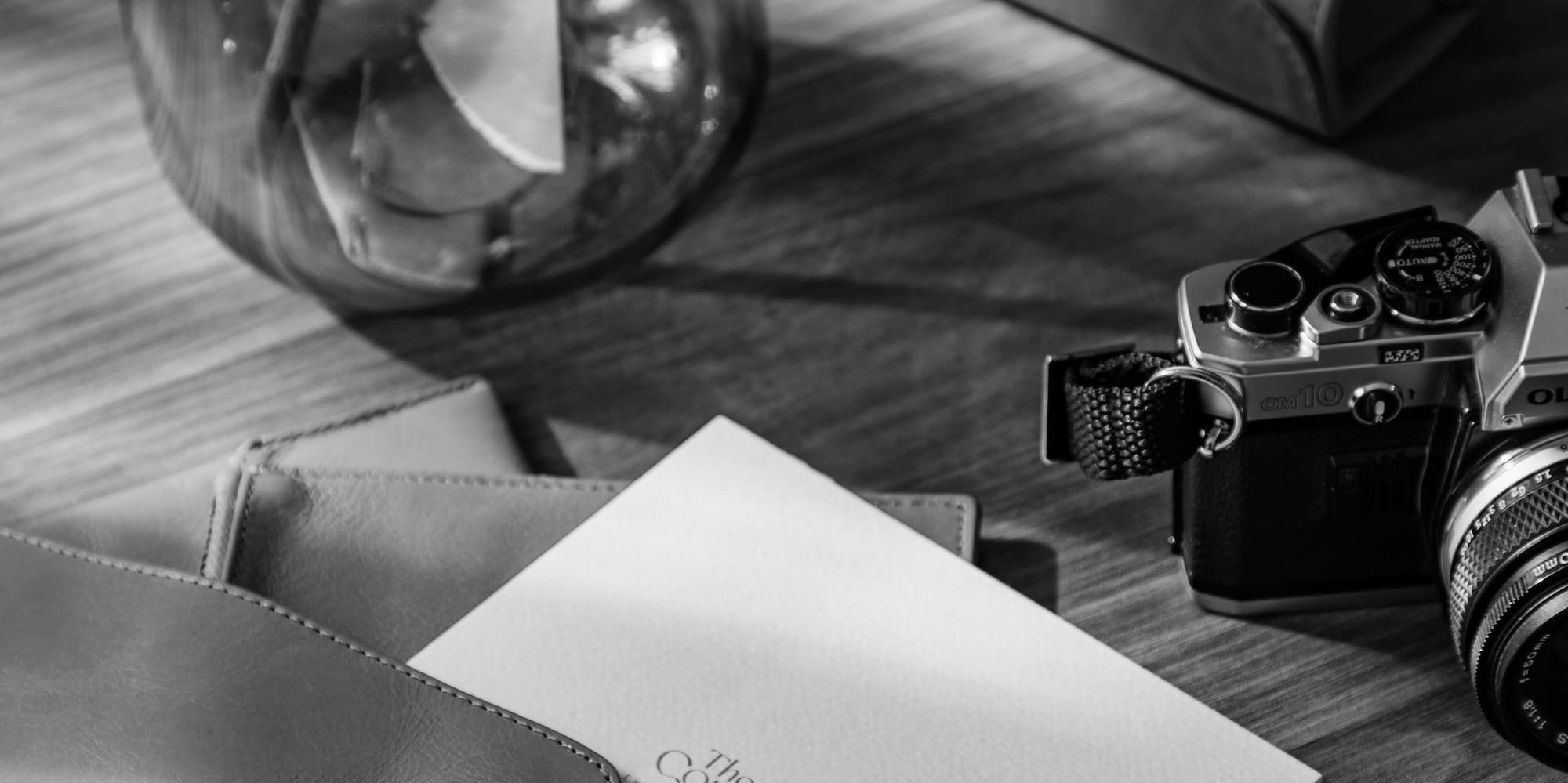 B&W Olympus OM10 camera, cotton, Meliá card, leather stationery, wooden desk.