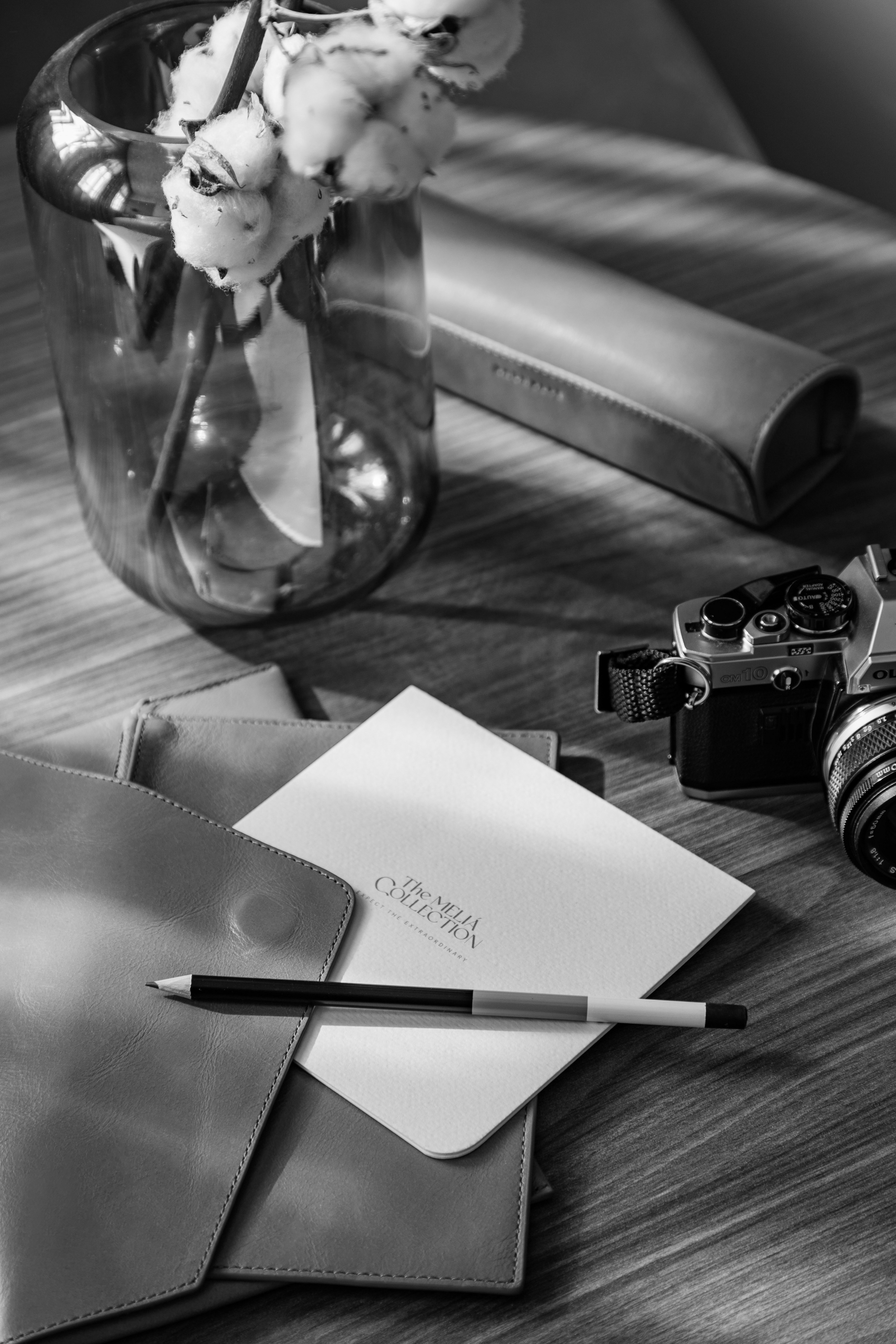 B&W Olympus OM10 camera, cotton, Meliá card, leather stationery, wooden desk.