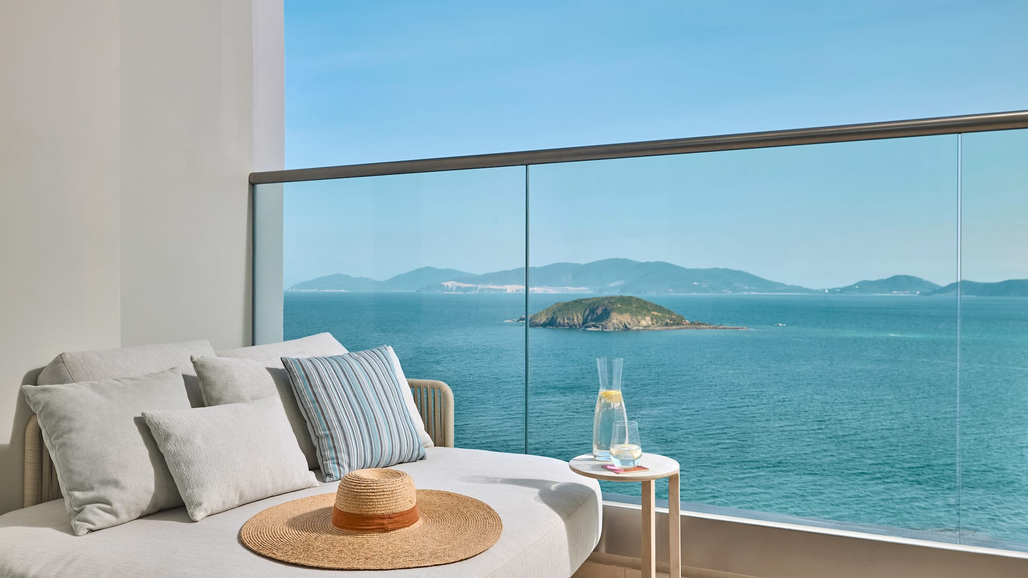 Luxury balcony lounge with panoramic ocean views and distant island.