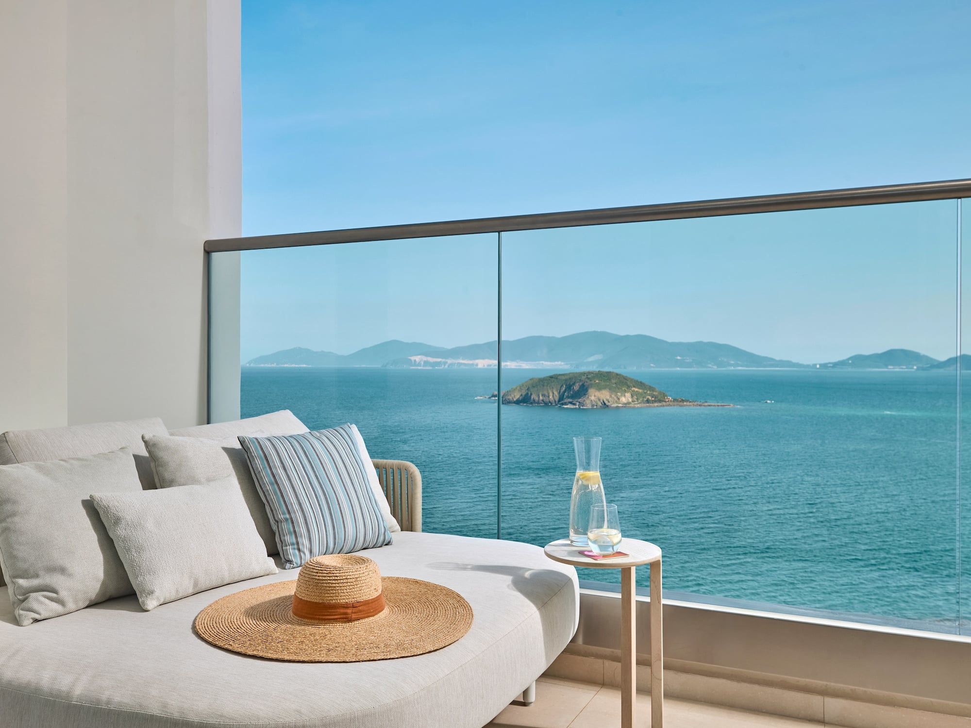 Ocean view balcony with lounge daybed, straw hat, and distant island.