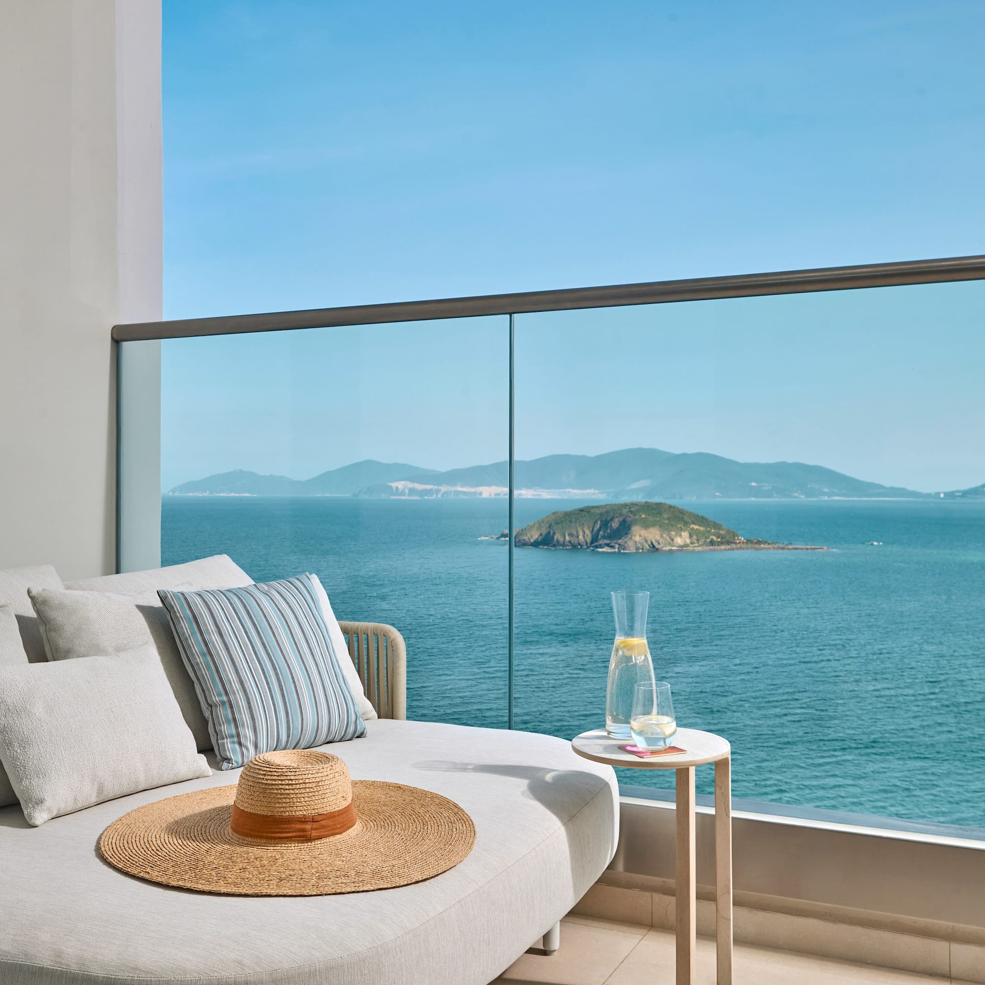 Luxury balcony lounge with panoramic ocean views and distant island.