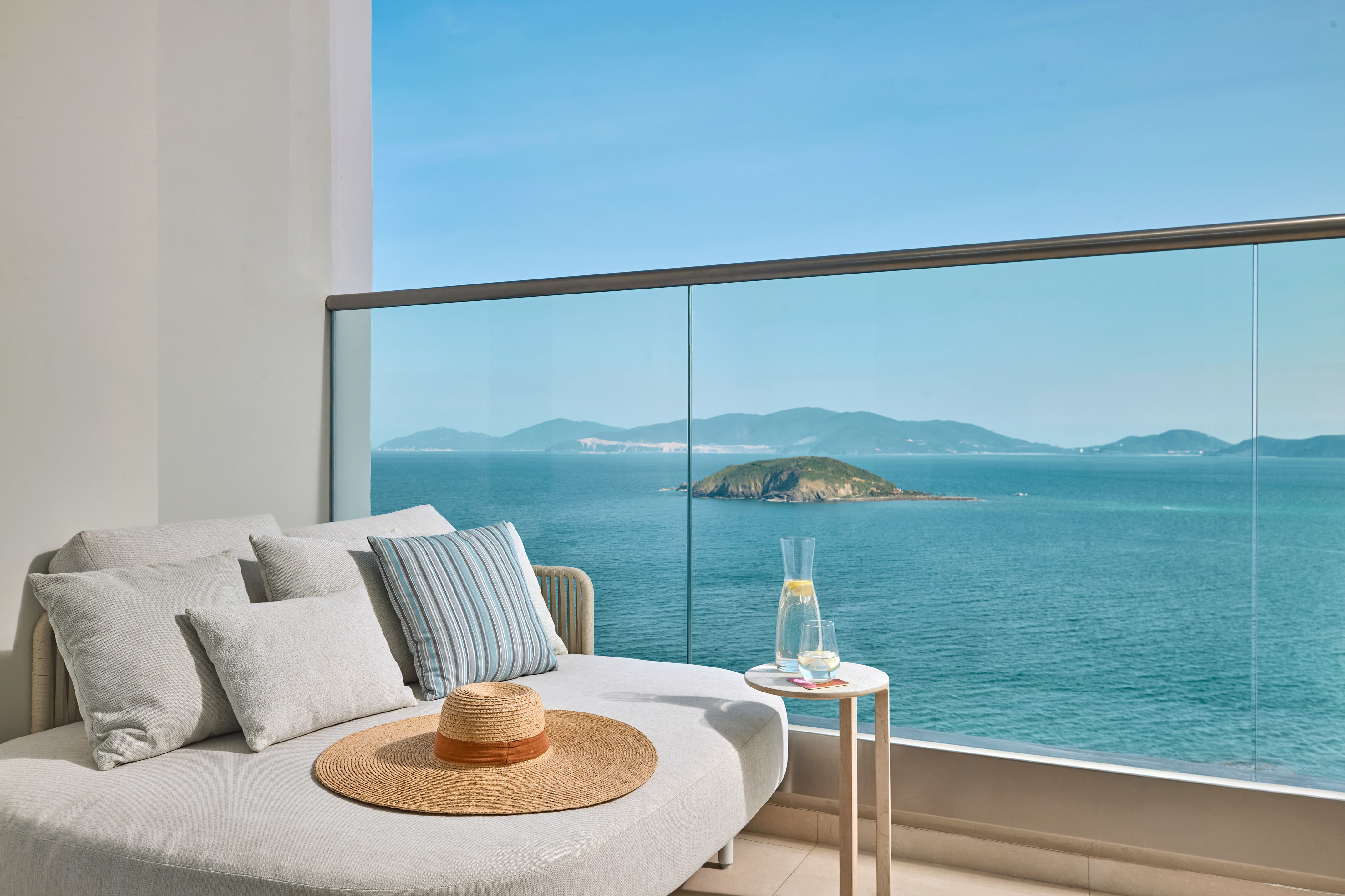 Luxury balcony lounge with panoramic ocean views and distant island.
