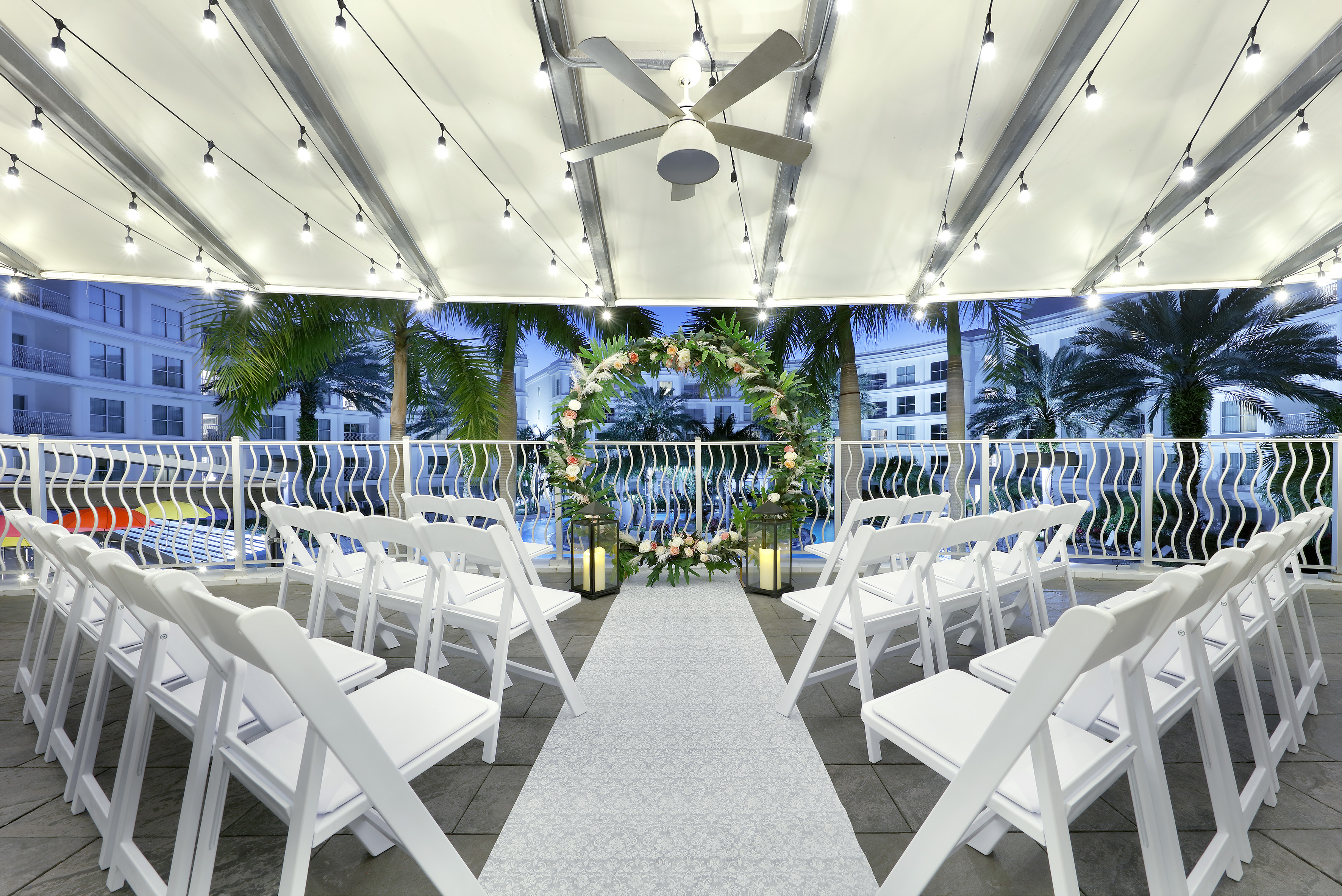 Tropical outdoor wedding ceremony with floral arch, white chairs, string lights. - The Pearl (circular floor plan) - Meliá Orlando Celebration, Orlando
