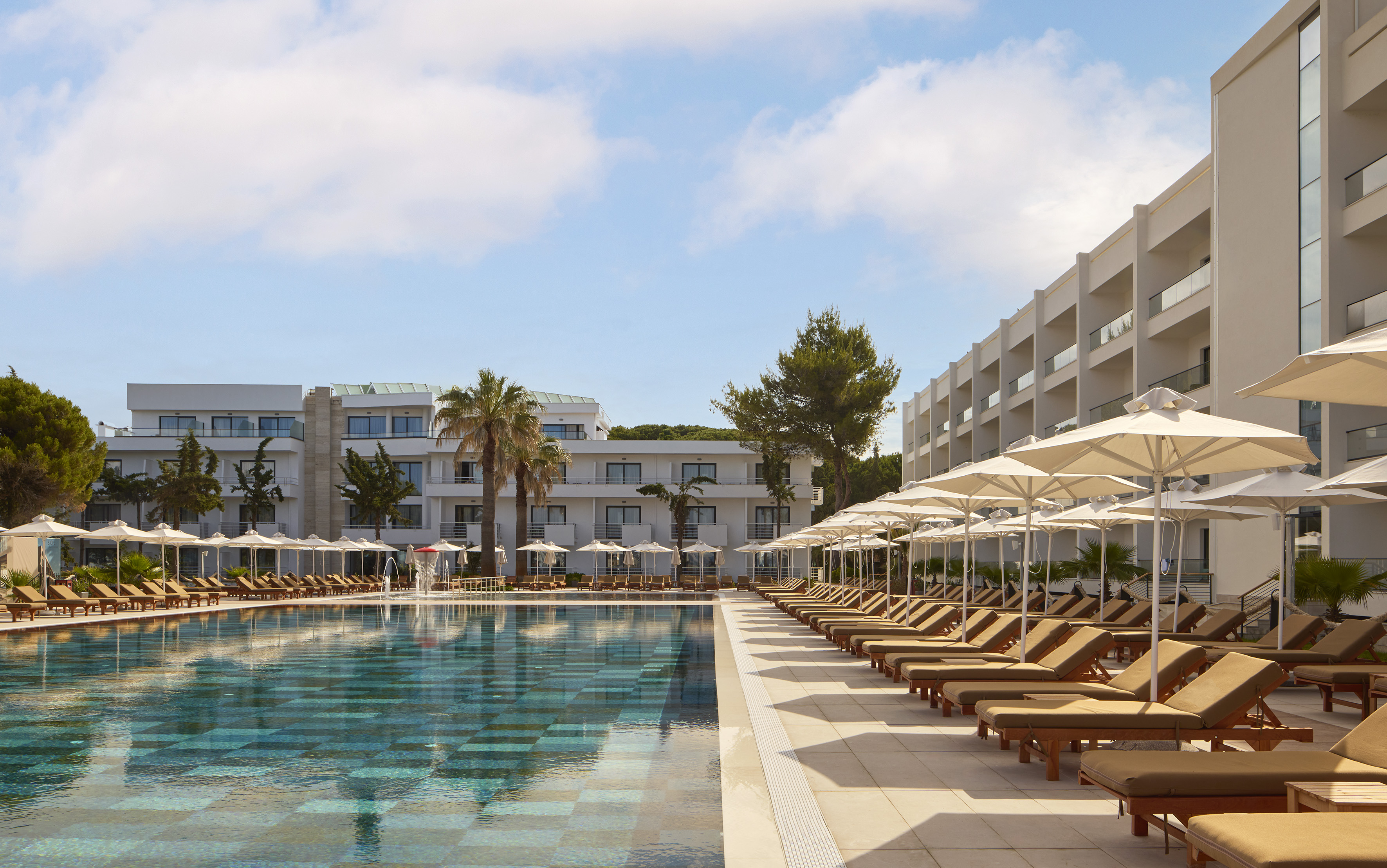 Resort swimming pool with sun loungers, umbrellas, and hotel buildings.