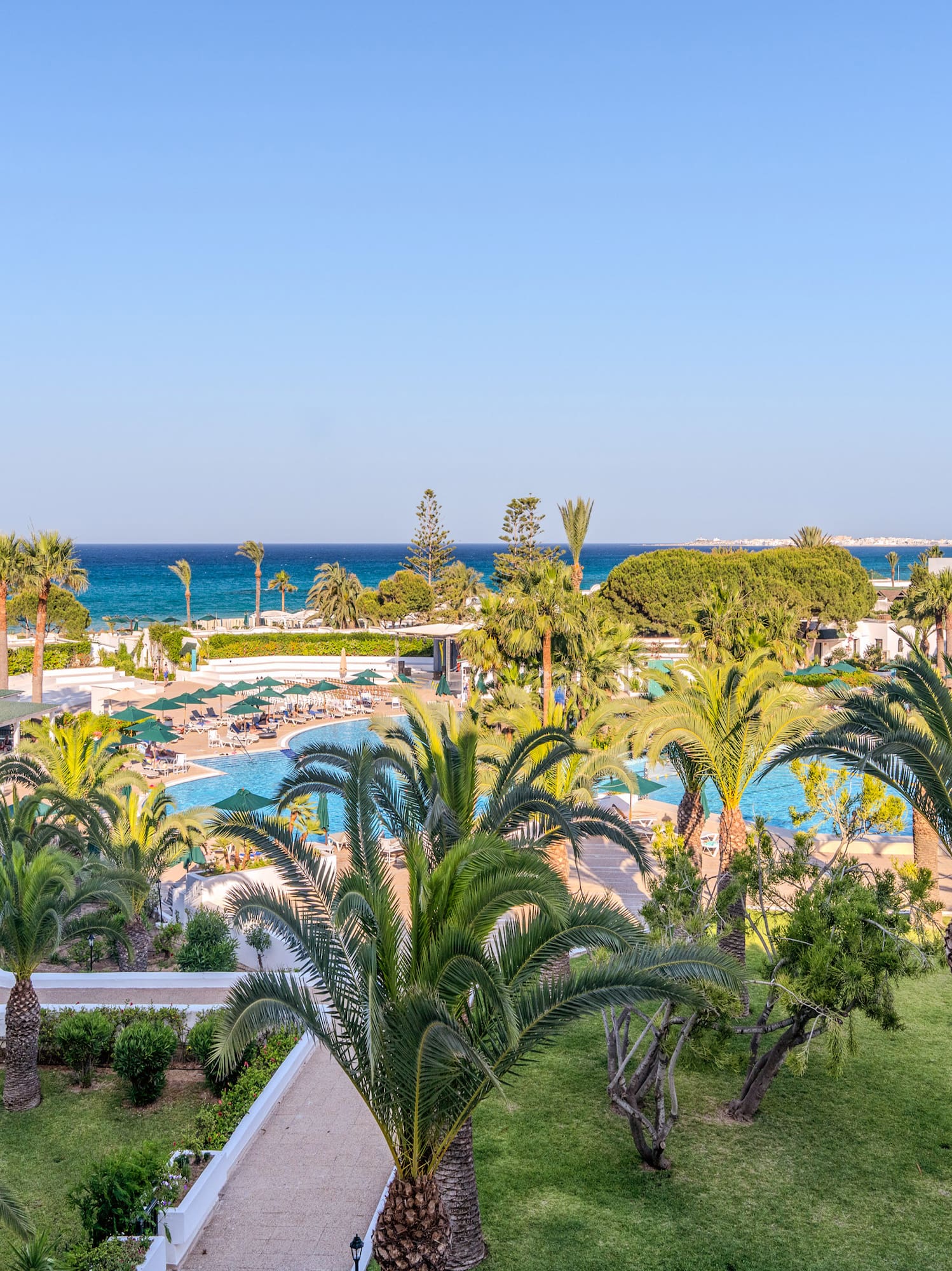 Resort con piscinas, toboganes acuáticos, palmeras, jardines y mar azul.