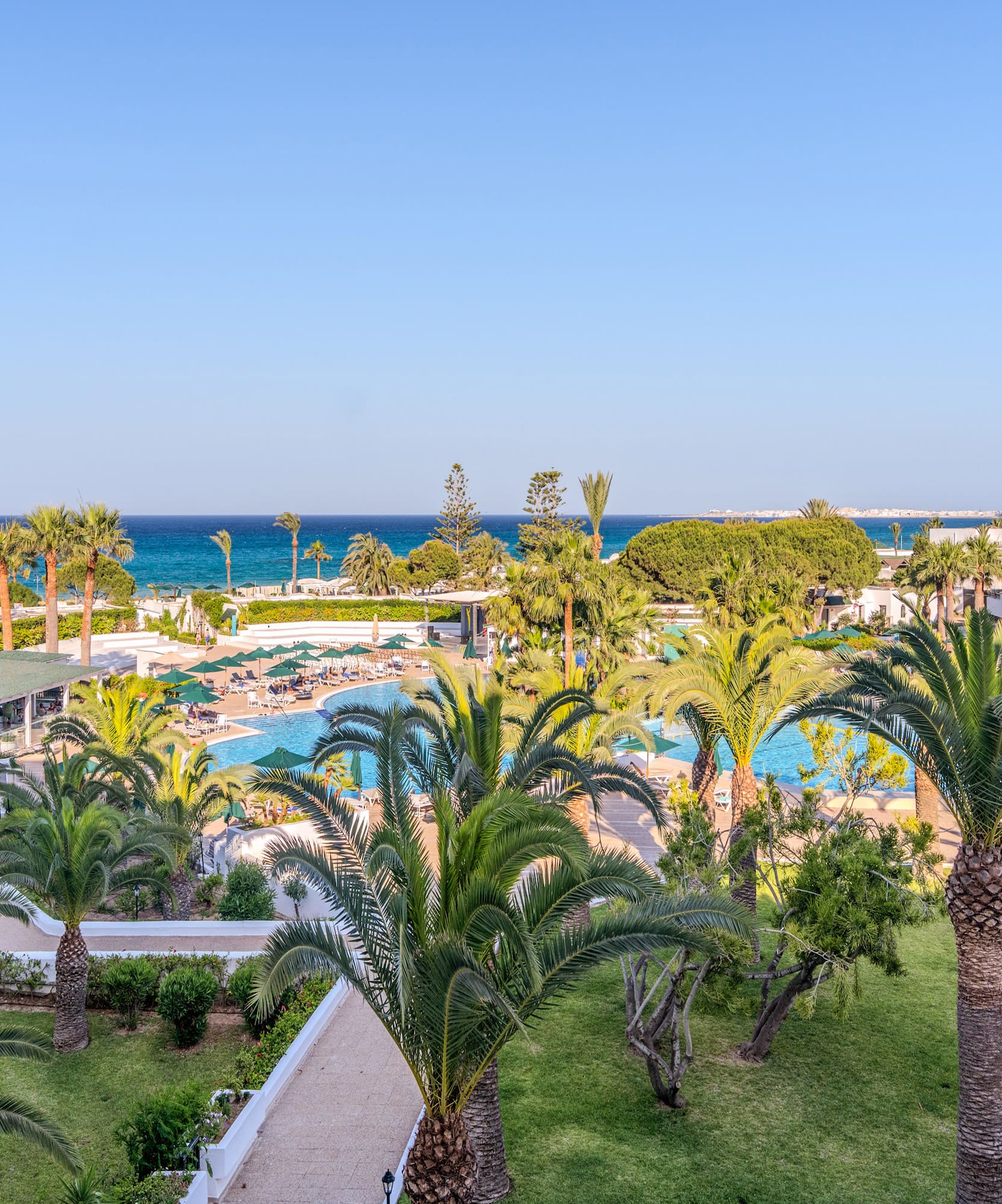 Resort con piscinas, toboganes acuáticos, palmeras, jardines y mar azul.