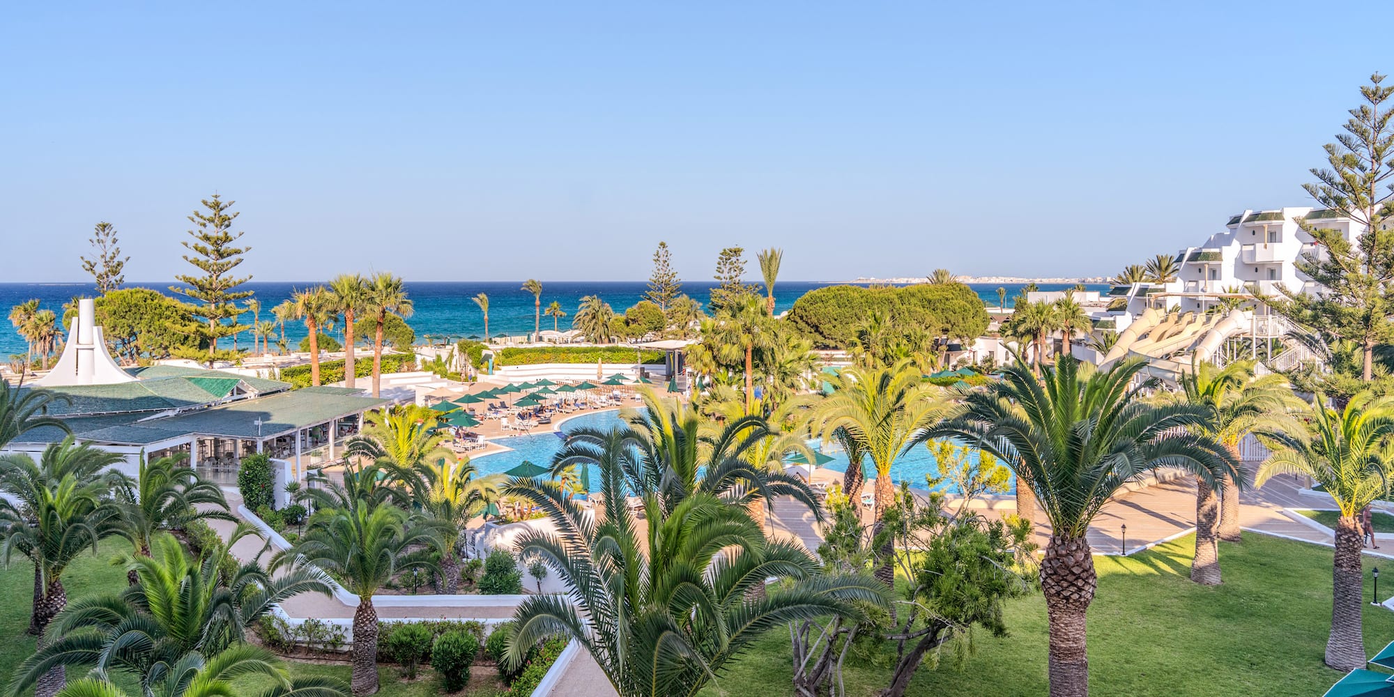 Hotel de playa con palmeras, piscinas, toboganes y vistas al mar.