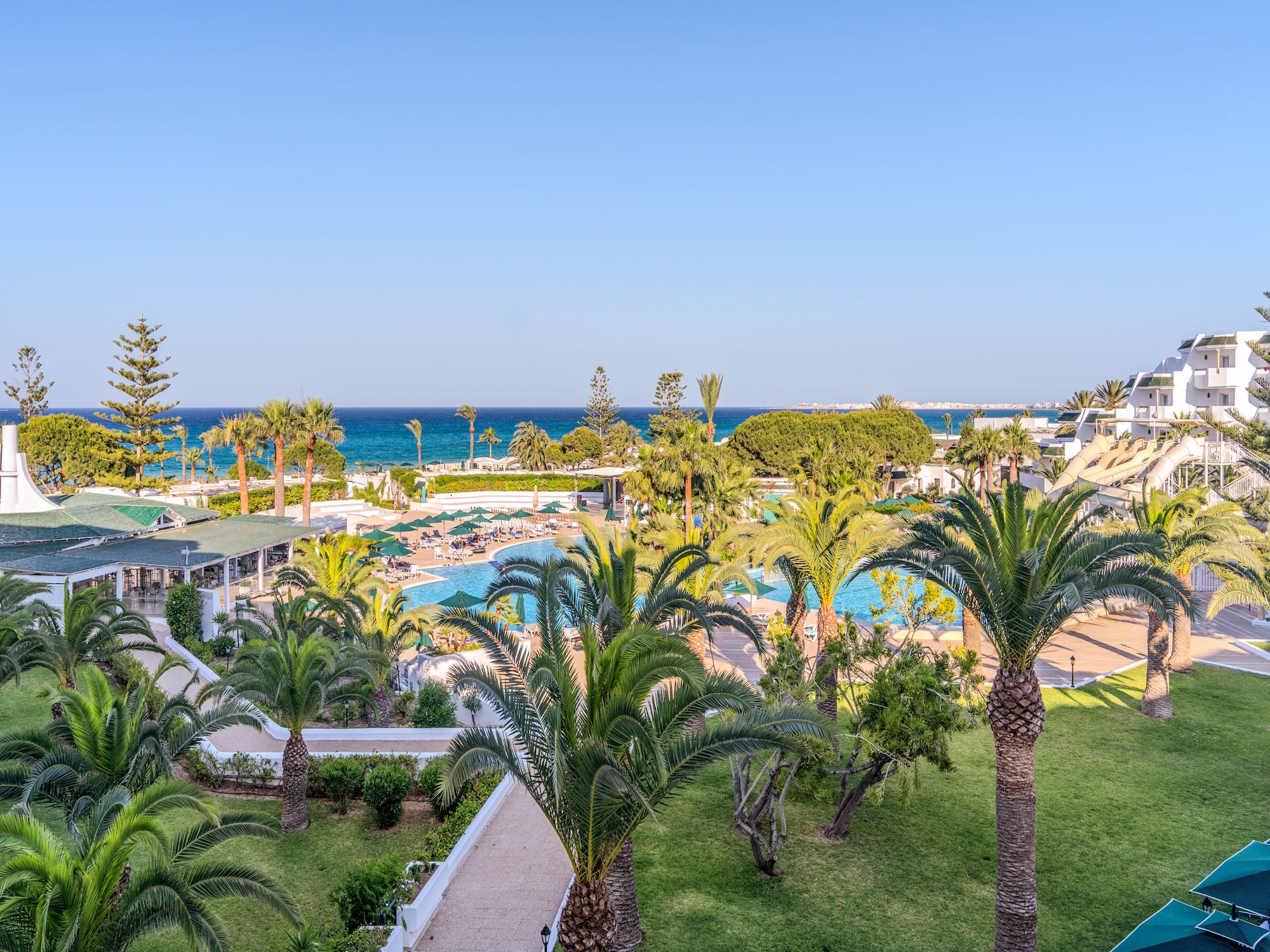 Hotel de playa con palmeras, piscinas, toboganes y vistas al mar.