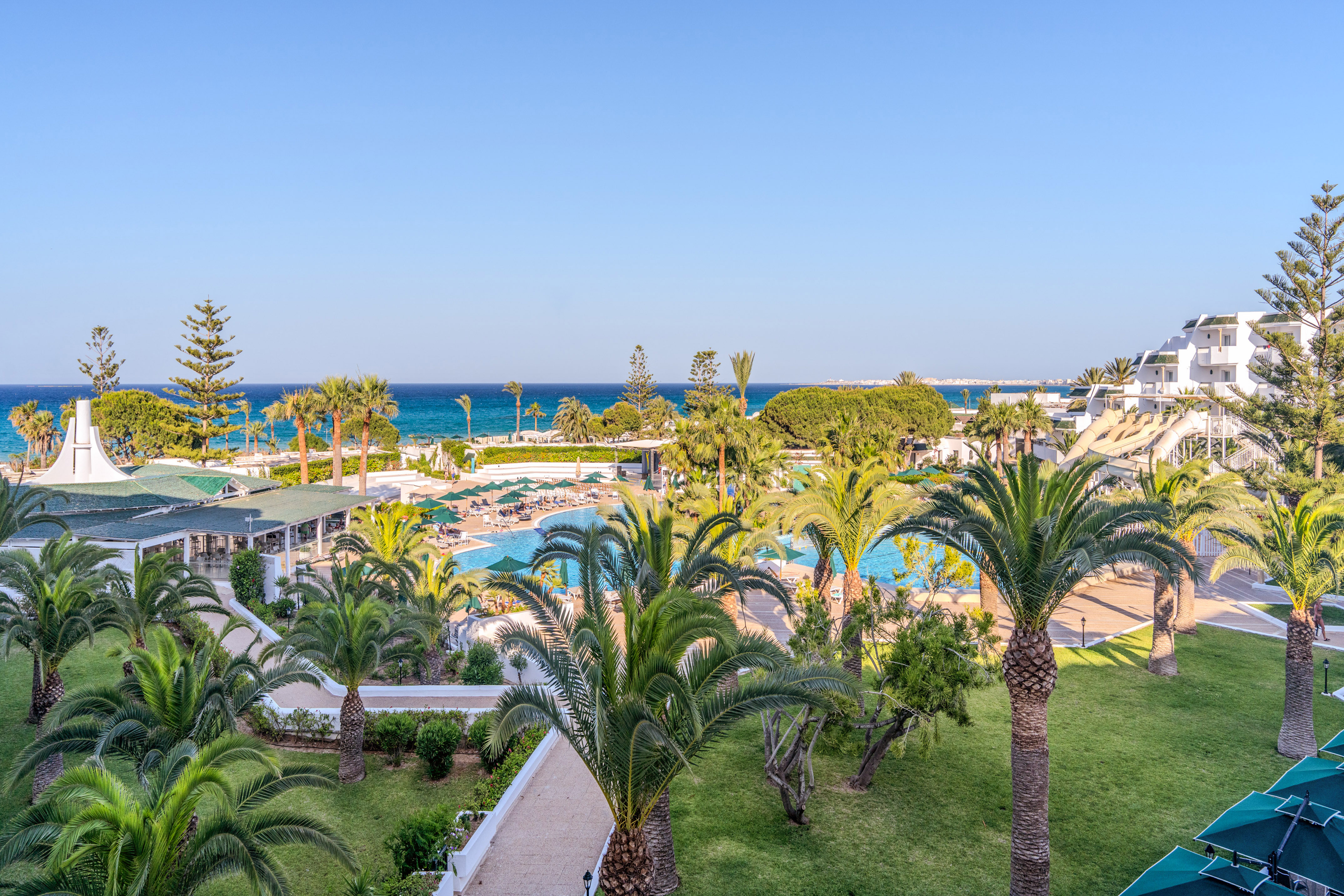 Hotel de playa con palmeras, piscinas, toboganes y vistas al mar.