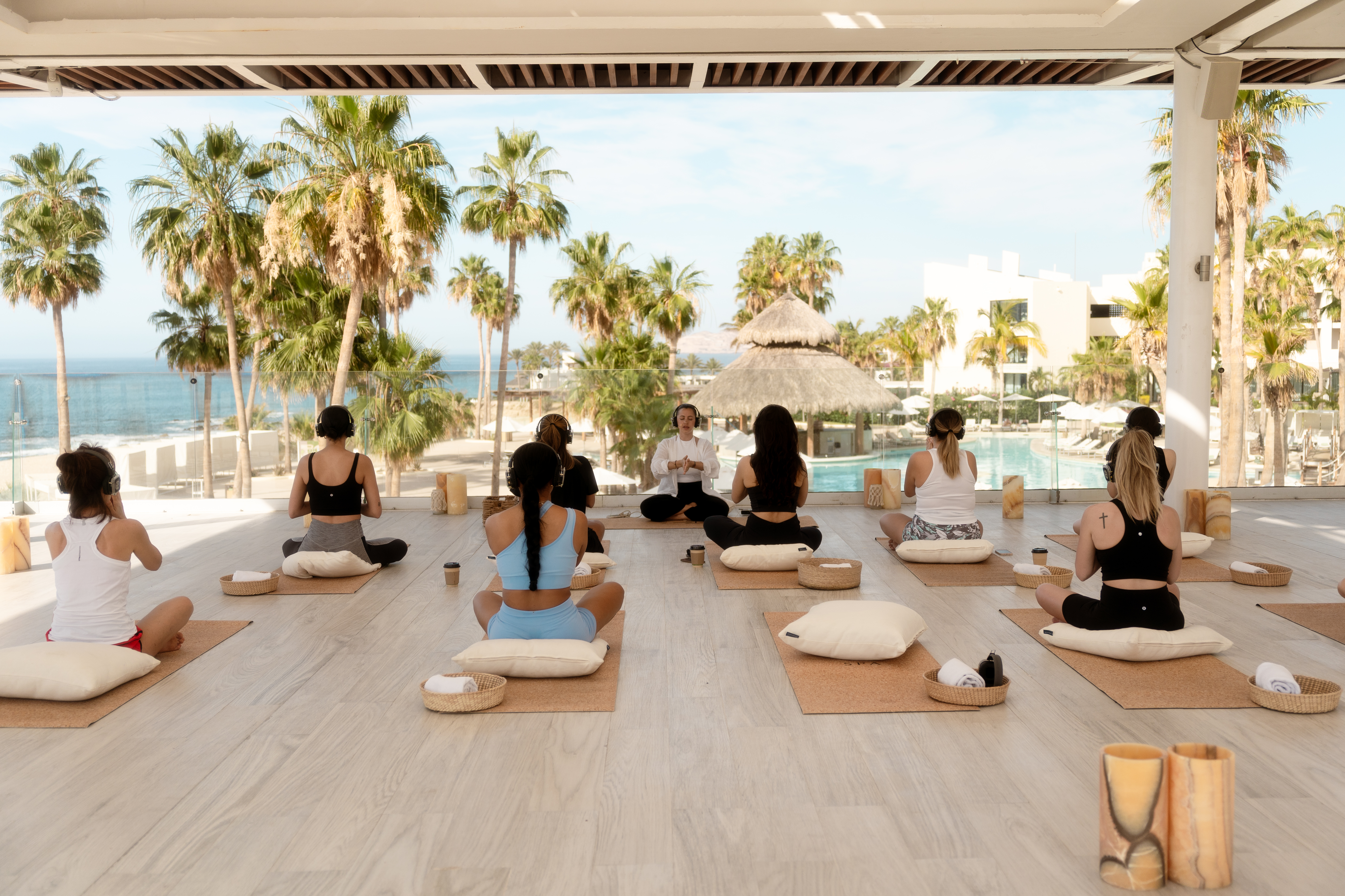 Outdoor group meditation session with headphones at a tropical beach resort.