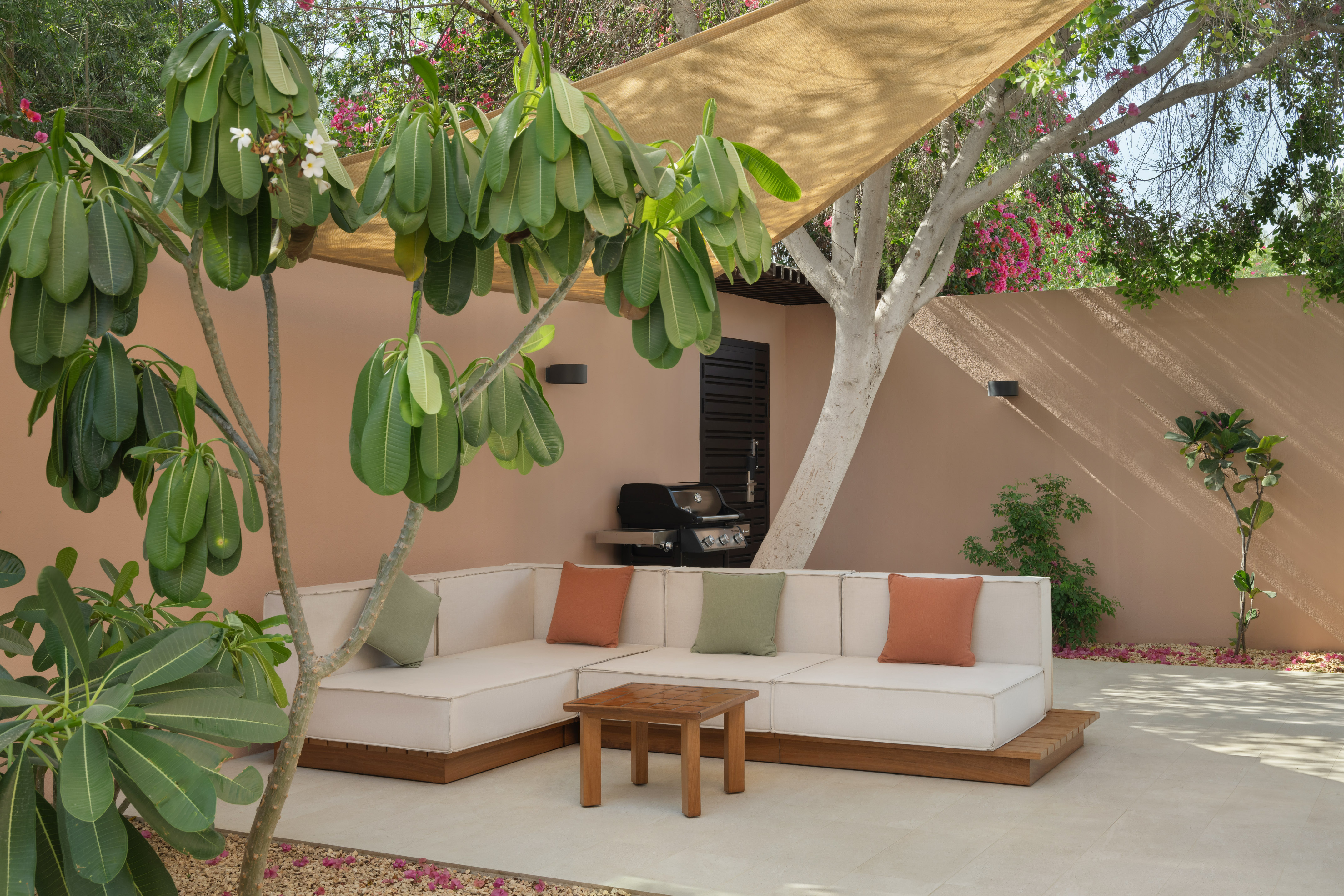 Modern outdoor patio with L-shaped sofa, coffee table, BBQ, and shade.