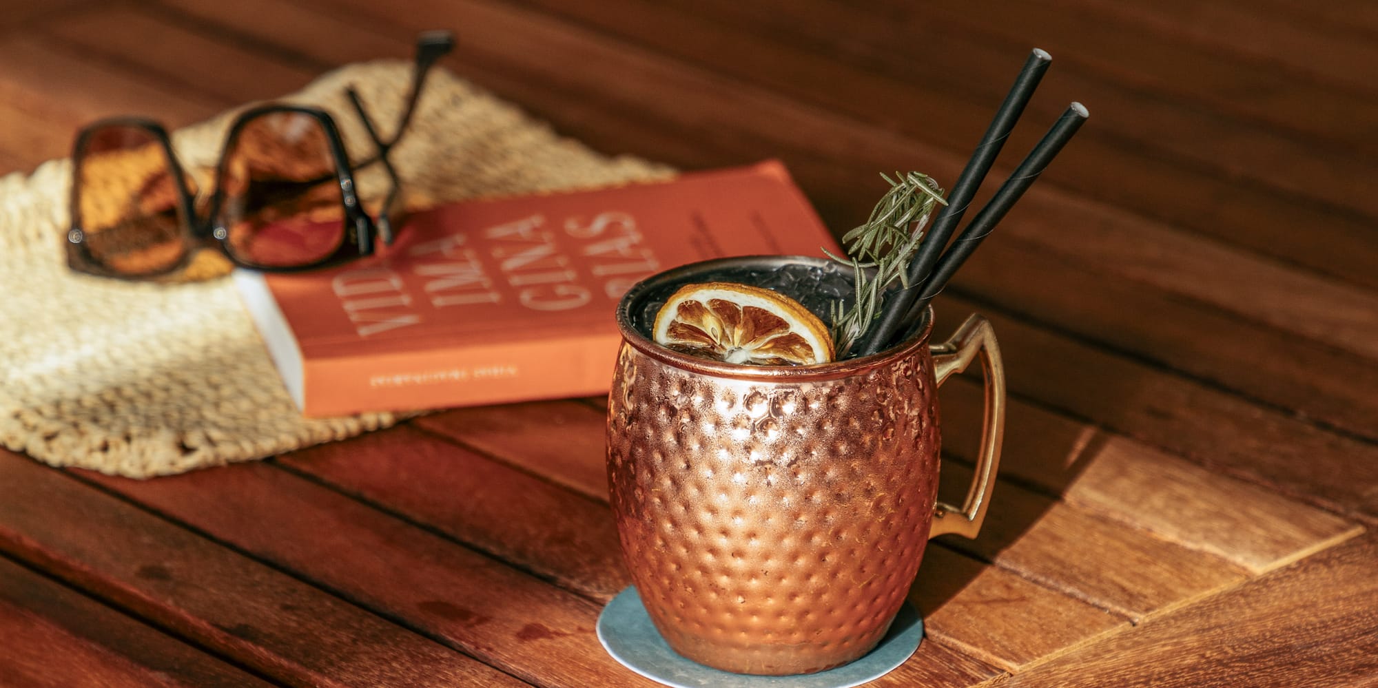 a copper mug with straws and a lemon slice on a wooden table